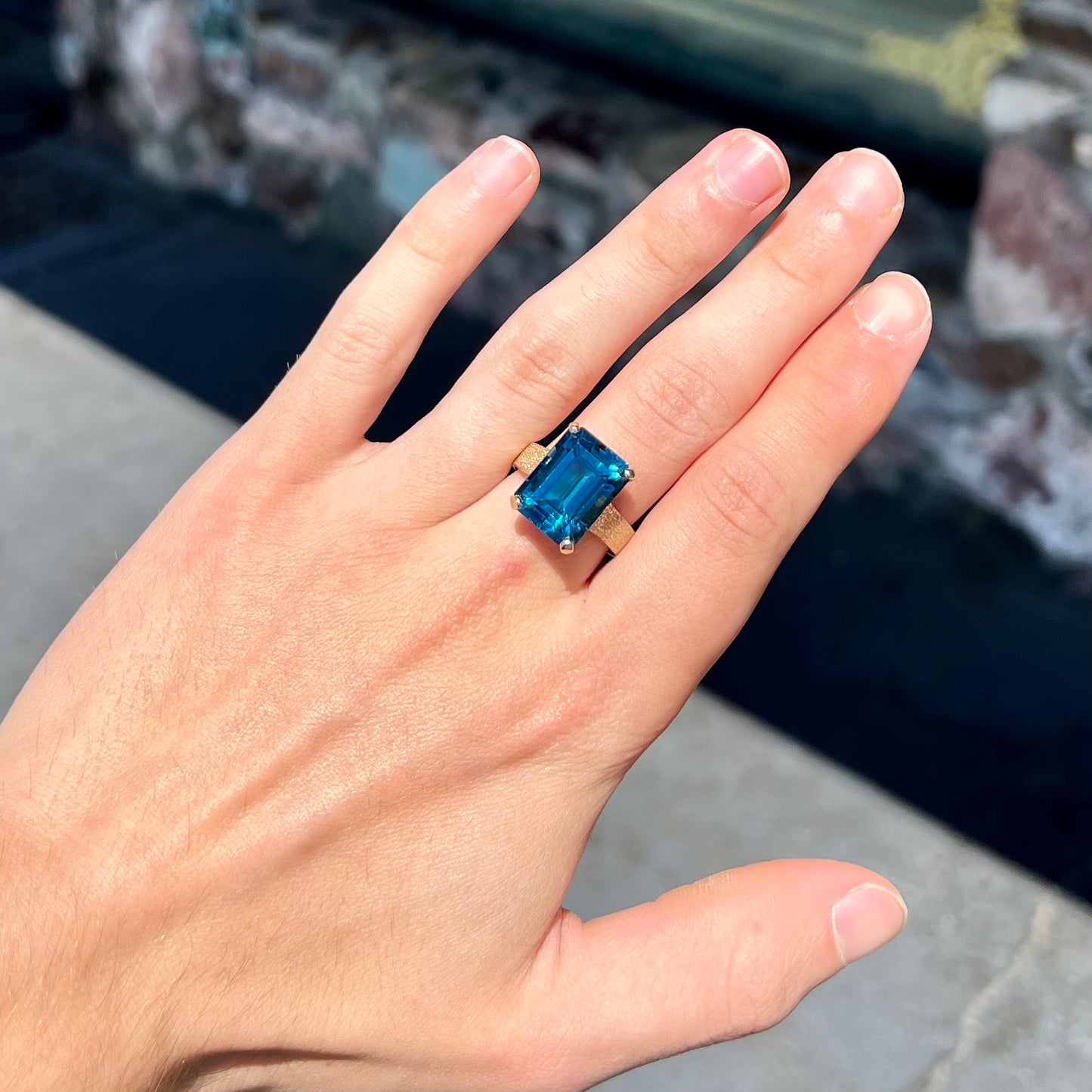 A ladies' yellow gold London blue topaz solitaire ring. The ring is textured, and the topaz is emerald cut.