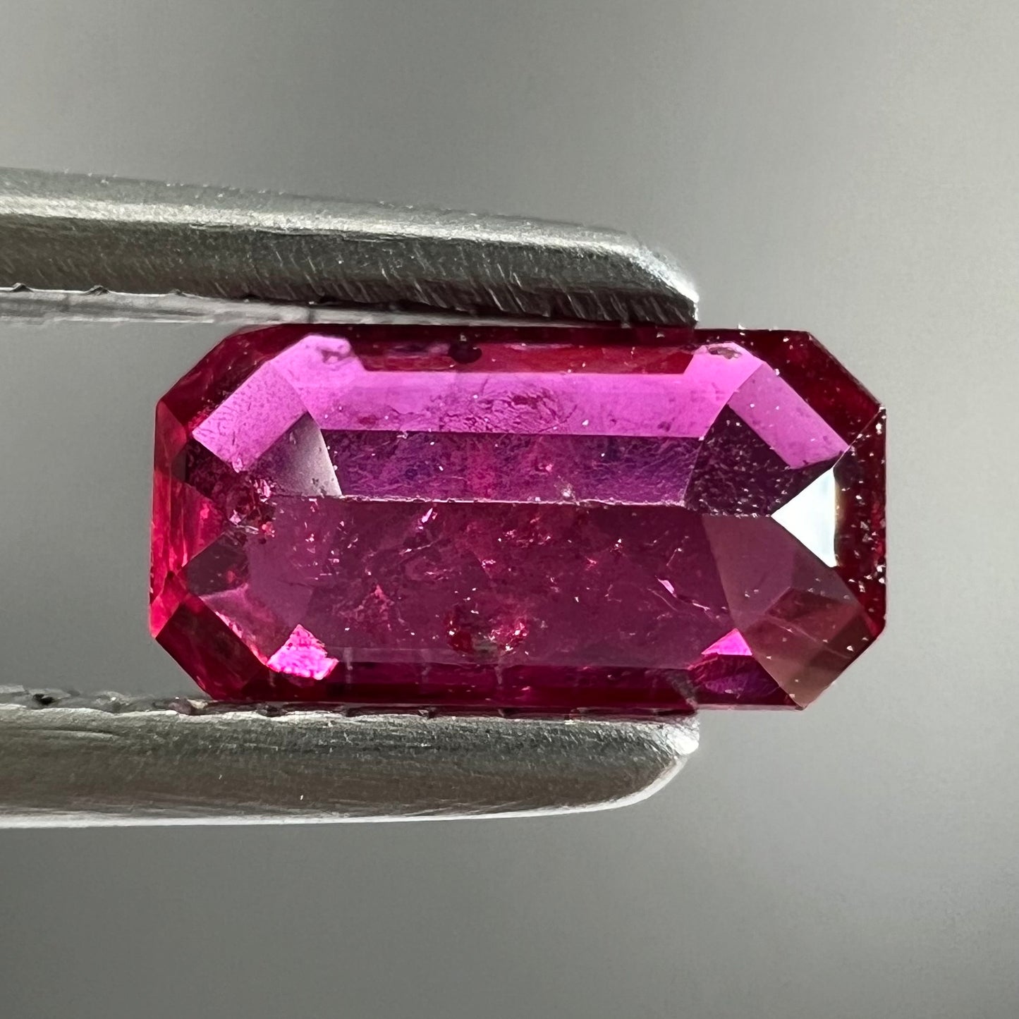 A loose, purplish red natural ruby gemstone. The stone is emerald cut.