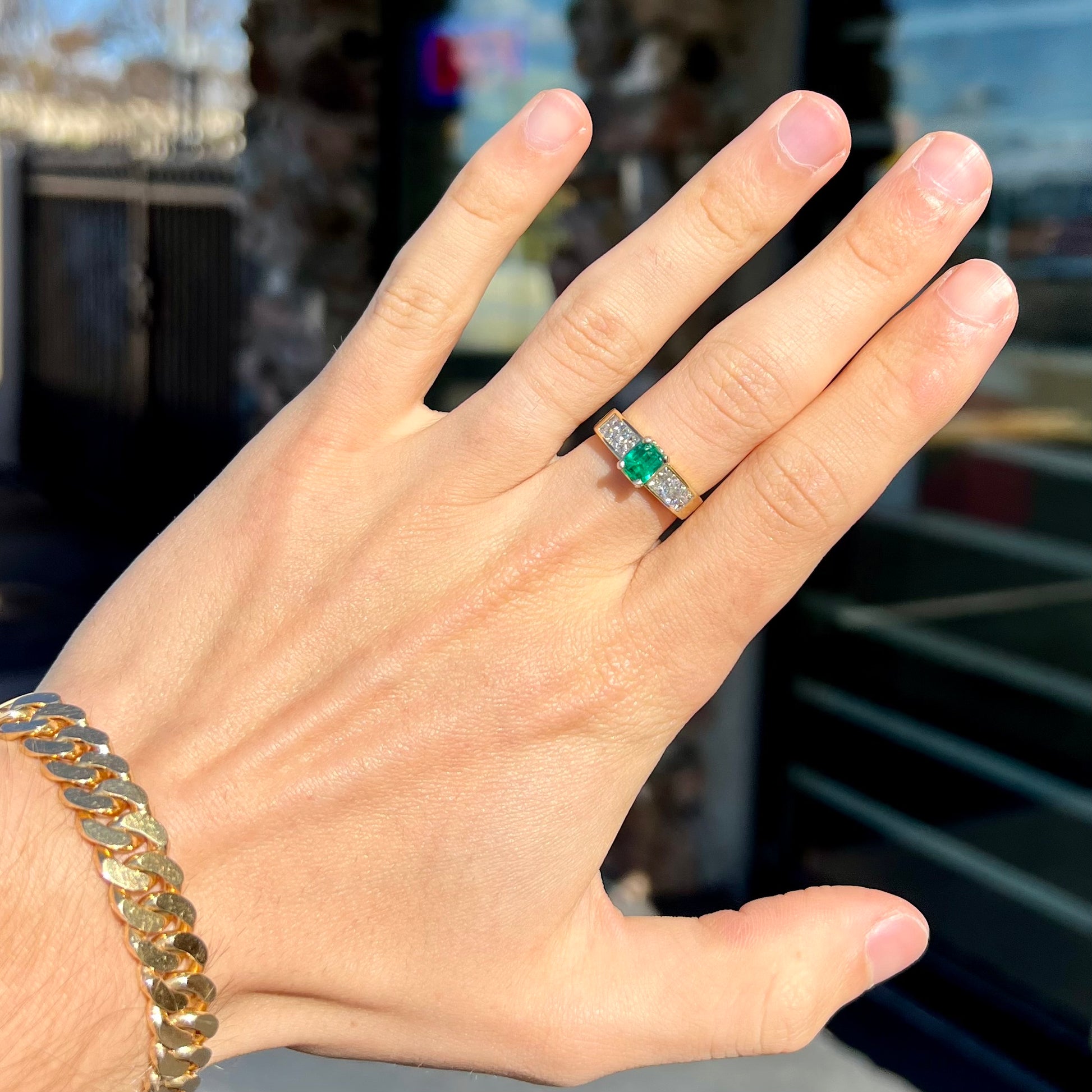 An 18 karat yellow gold ladies' emerald ring, channel set with princess cut diamonds.