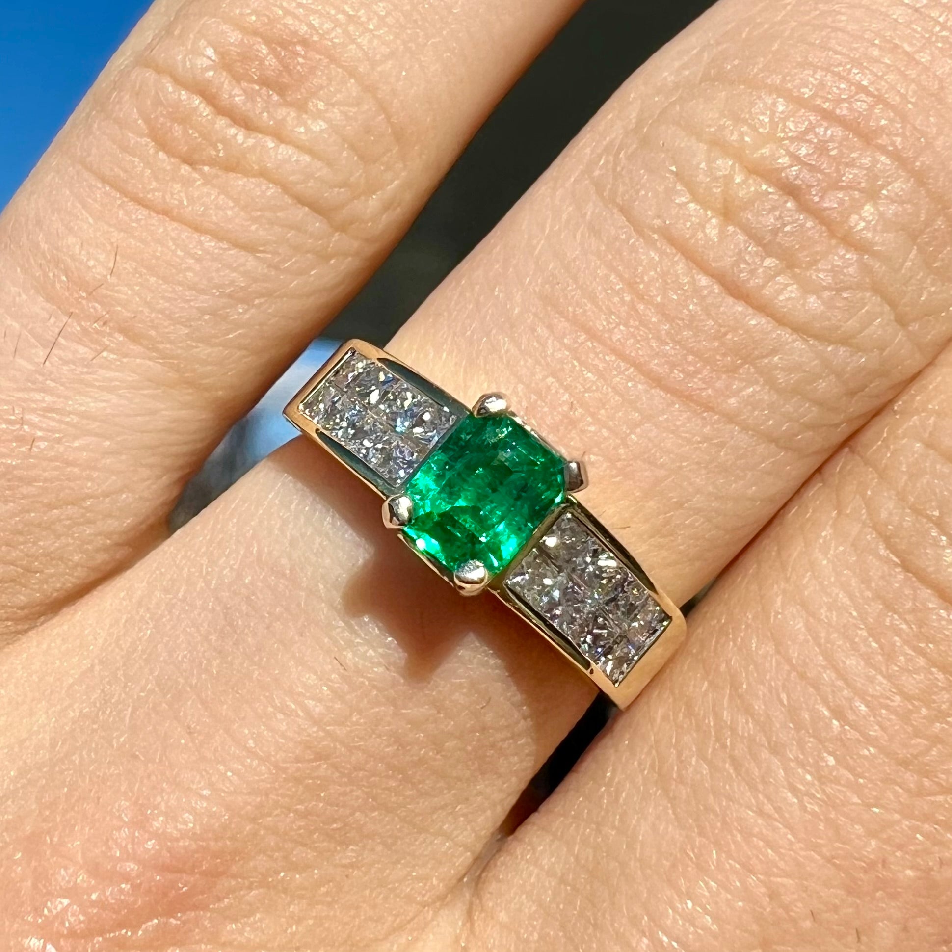 An 18 karat yellow gold ladies' emerald ring, channel set with princess cut diamonds.
