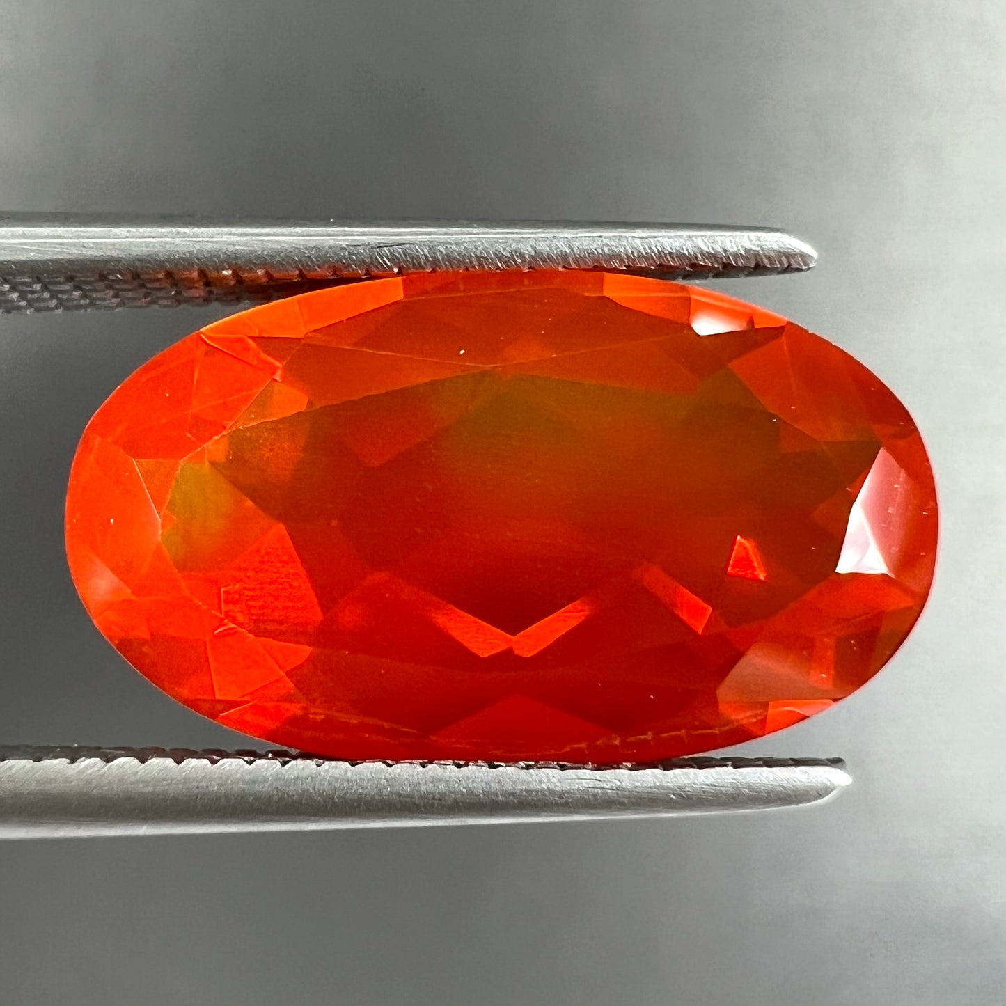 A loose, faceted oval cut Mexican fire opal stone. The stone is a bright orange color.