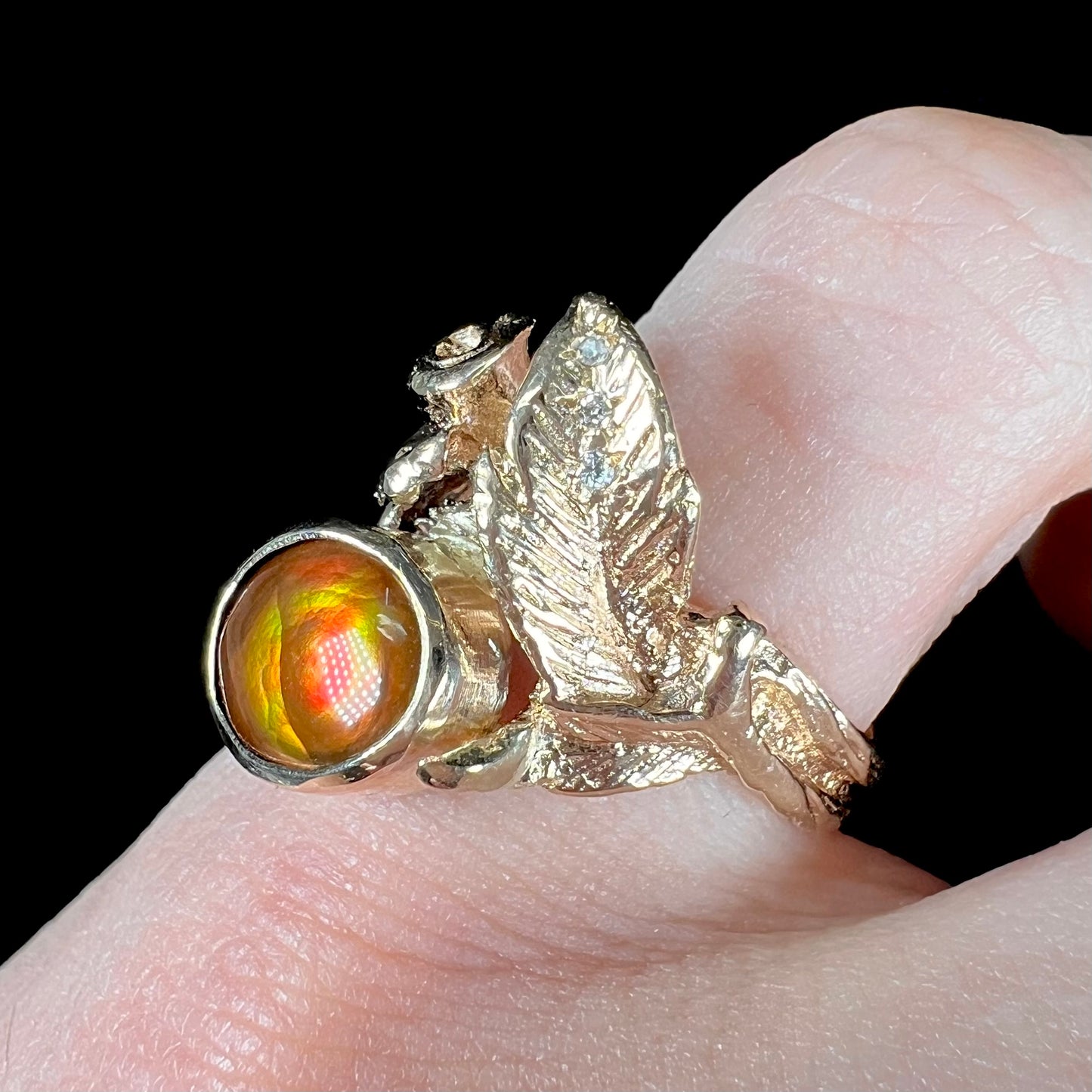 A ladies' yellow gold flower style ring set with an oval cabochon cut fire agate and diamond accents.