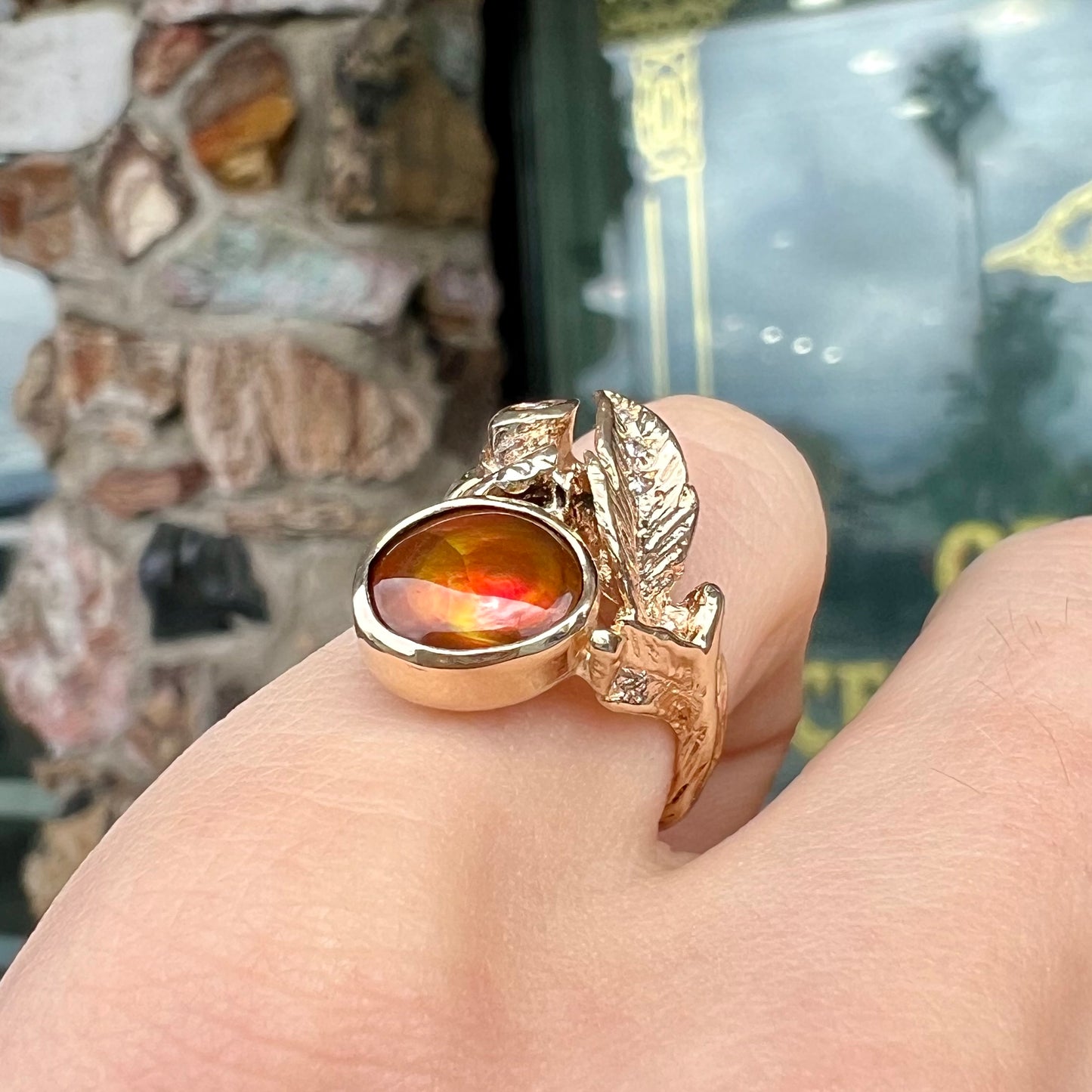 A ladies' yellow gold flower style ring set with an oval cabochon cut fire agate and diamond accents.