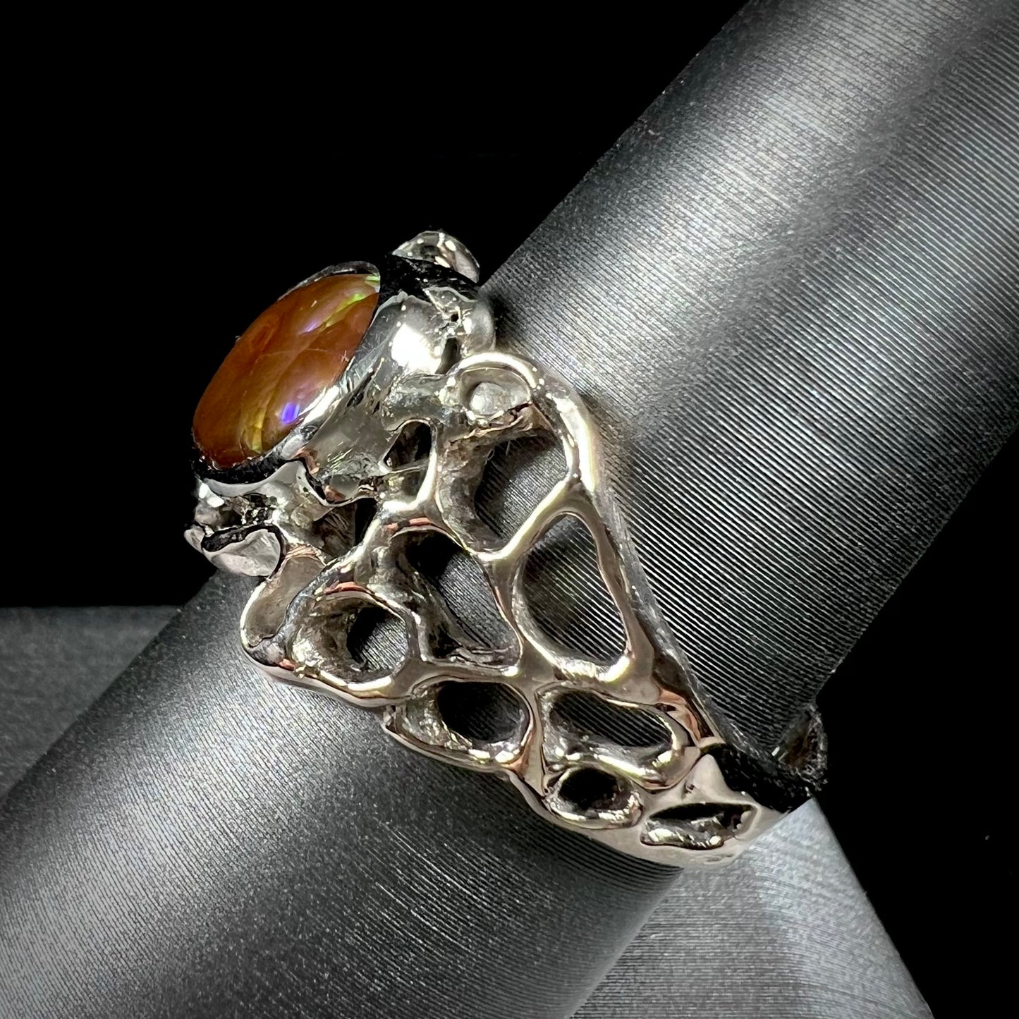 An organic-style white gold men's ring, bezel set with an oval cut Mexican fire agate stone.  The stone is green and purple.