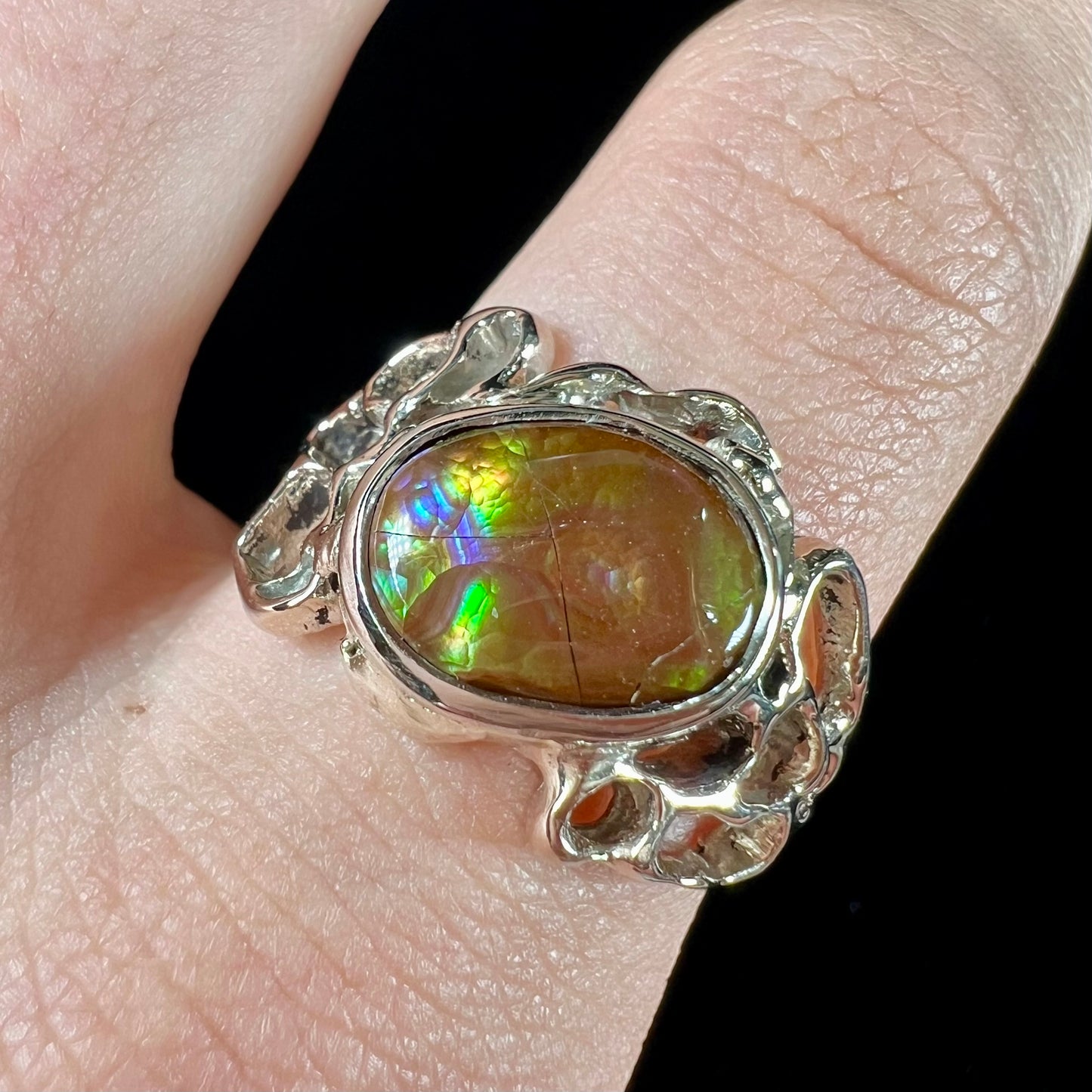 An organic-style white gold men's ring, bezel set with an oval cut Mexican fire agate stone.  The stone is green and purple.