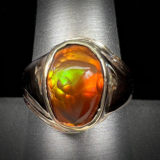 A men's yellow gold solitaire ring set with an oval cabochon cut fire agate stone.  The stone is red and green.