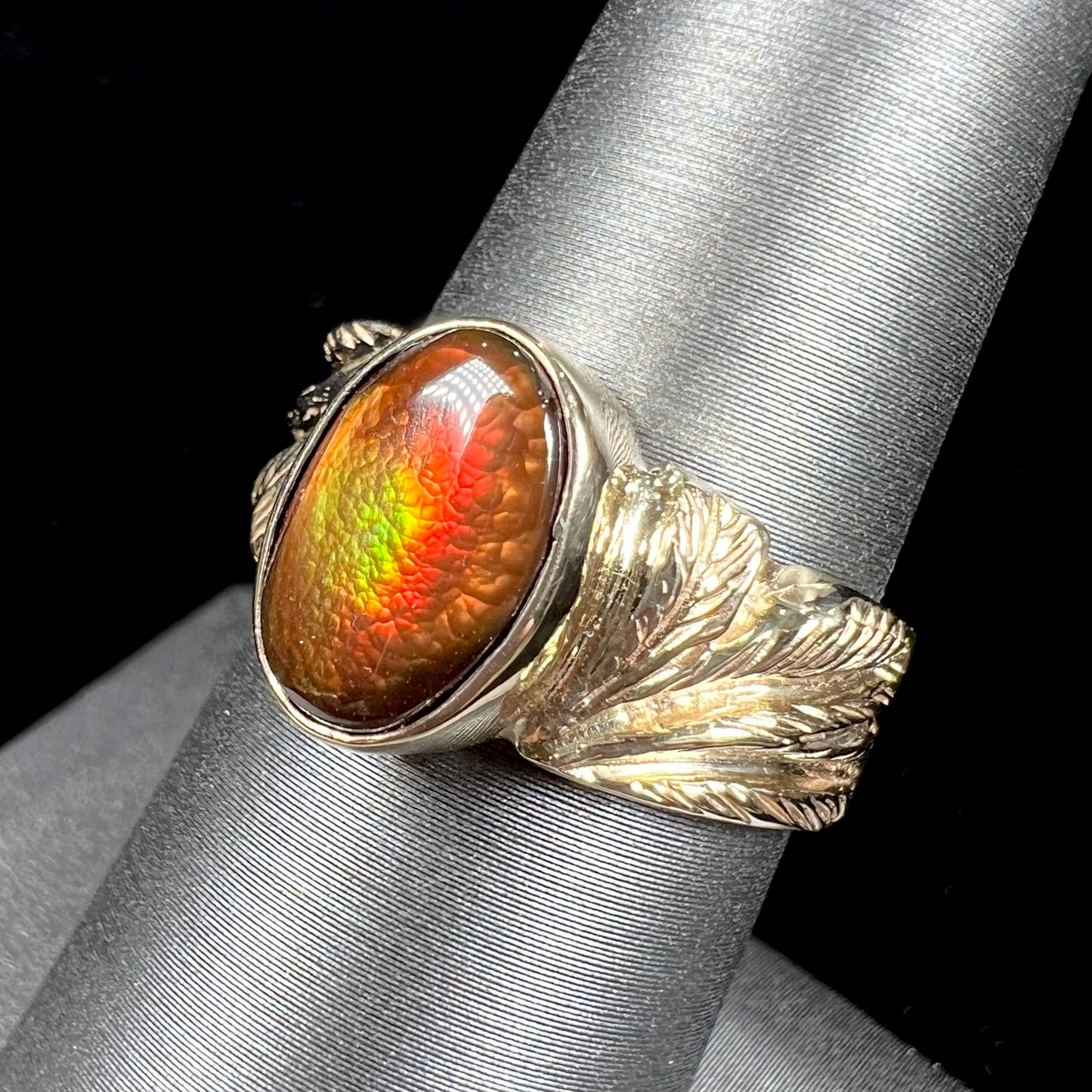 A unisex oval cabochon cut fire agate ring cast in yellow gold. The stone flashes green and red colors.