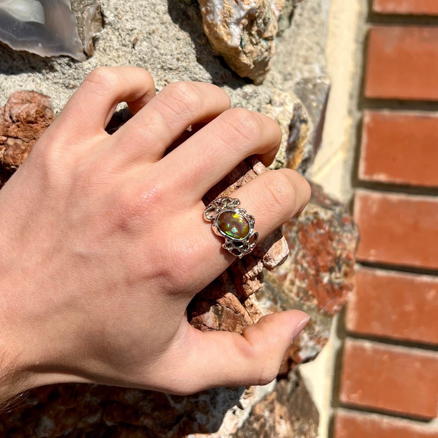 An organic-style white gold men's ring, bezel set with an oval cut Mexican fire agate stone.  The stone is green and purple.