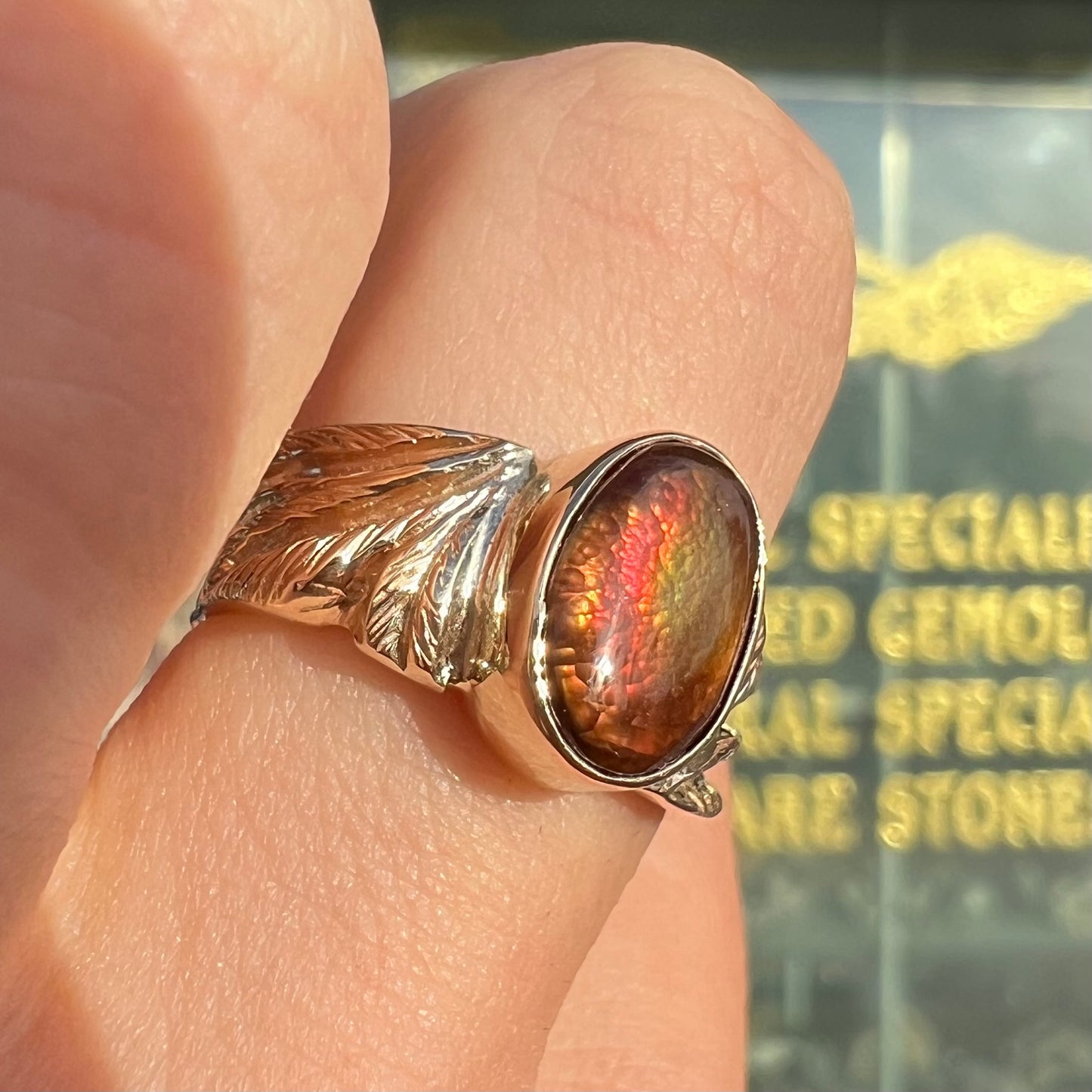 A unisex oval cabochon cut fire agate ring cast in yellow gold. The stone flashes green and red colors.
