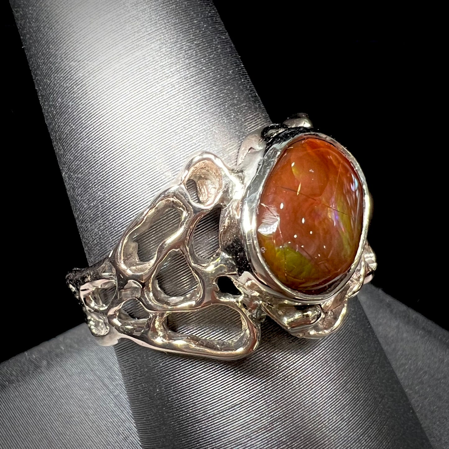 An organic-style white gold men's ring, bezel set with an oval cut Mexican fire agate stone.  The stone is green and purple.