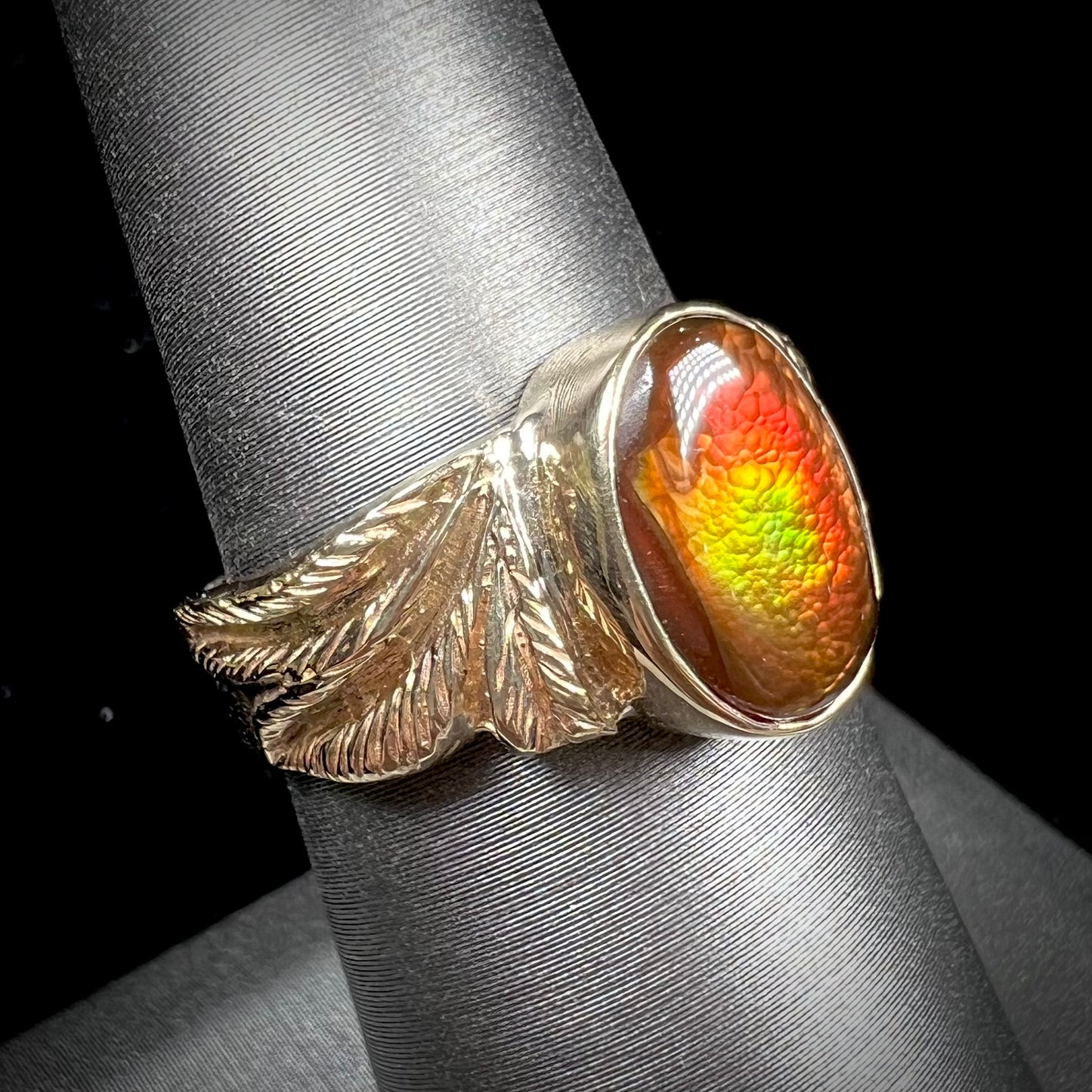 A unisex oval cabochon cut fire agate ring cast in yellow gold. The stone flashes green and red colors.