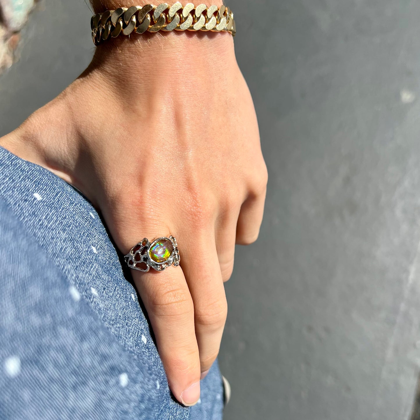 An organic-style white gold men's ring, bezel set with an oval cut Mexican fire agate stone.  The stone is green and purple.