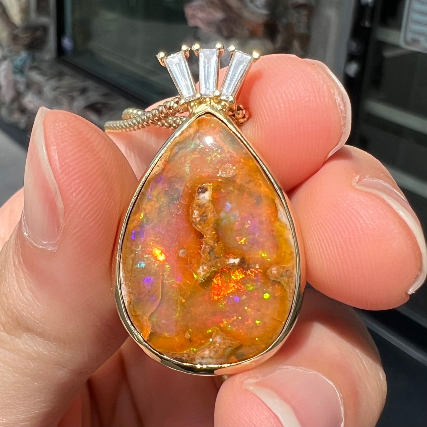 A unisex pear shaped fire opal pendant set with tapered baguette cut diamond accents in 18 karat gold.