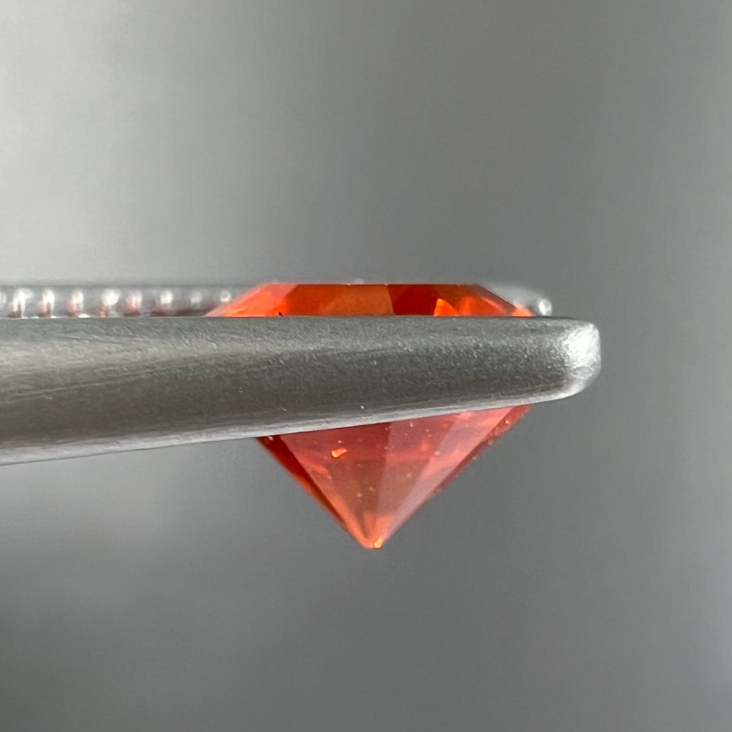 A faceted round cut natural Mexican fire opal stone. The stone is bright orange in color.