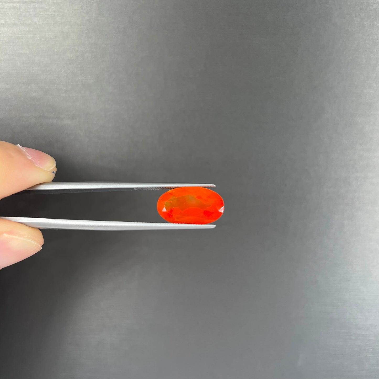 A loose, faceted oval cut Mexican fire opal stone. The stone is a bright orange color.