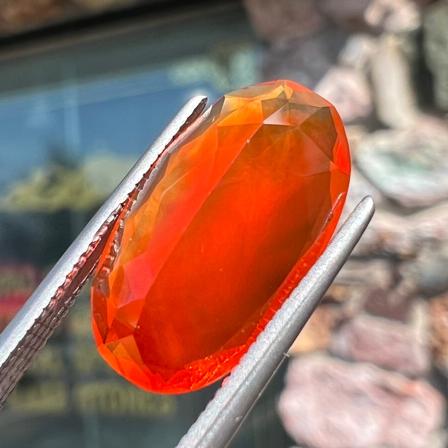 A loose, faceted oval cut Mexican fire opal stone. The stone is a bright orange color.