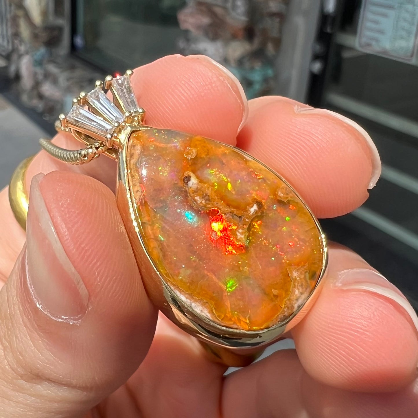 A unisex pear shaped fire opal pendant set with tapered baguette cut diamond accents in 18 karat gold.