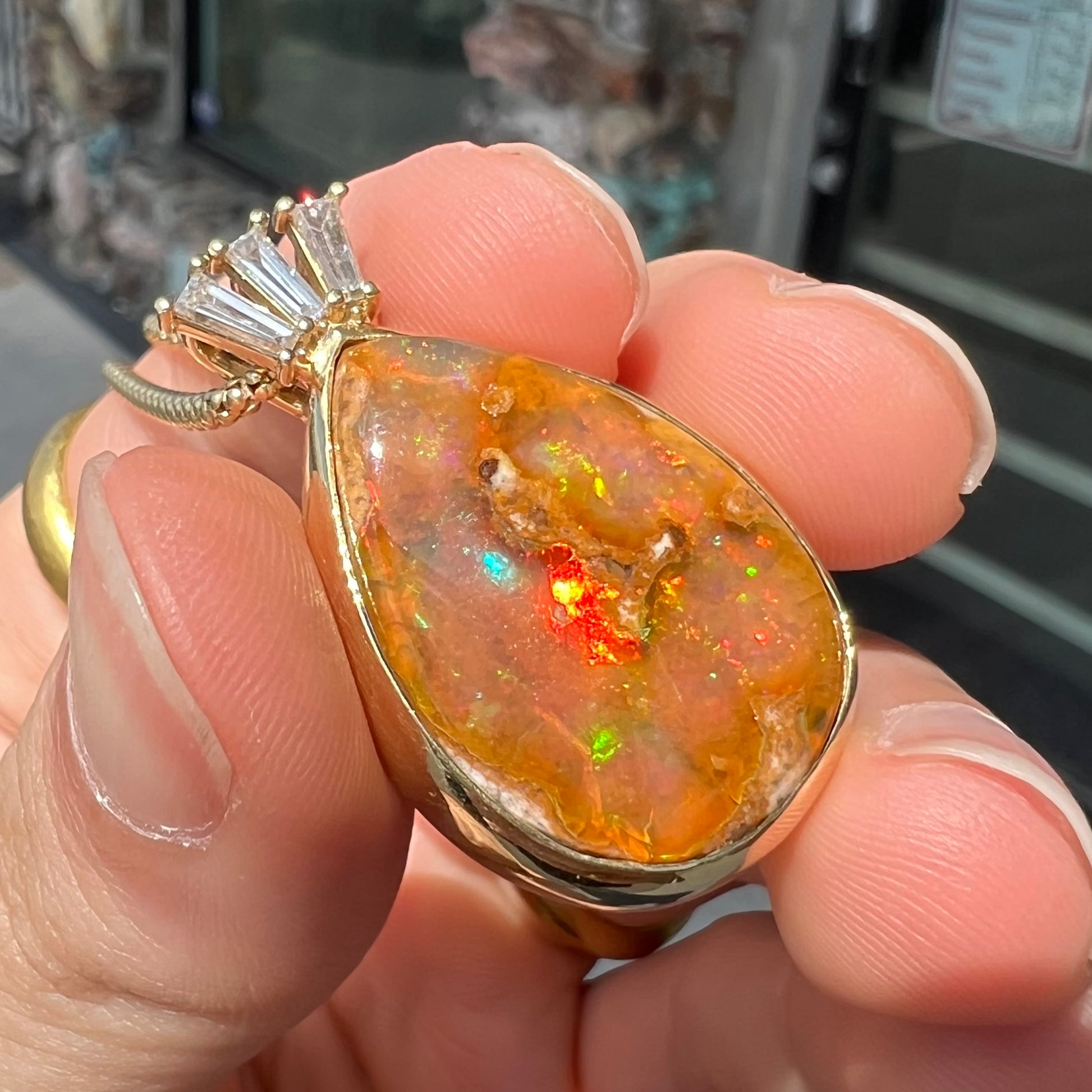 A unisex pear shaped fire opal pendant set with tapered baguette cut diamond accents in 18 karat gold.