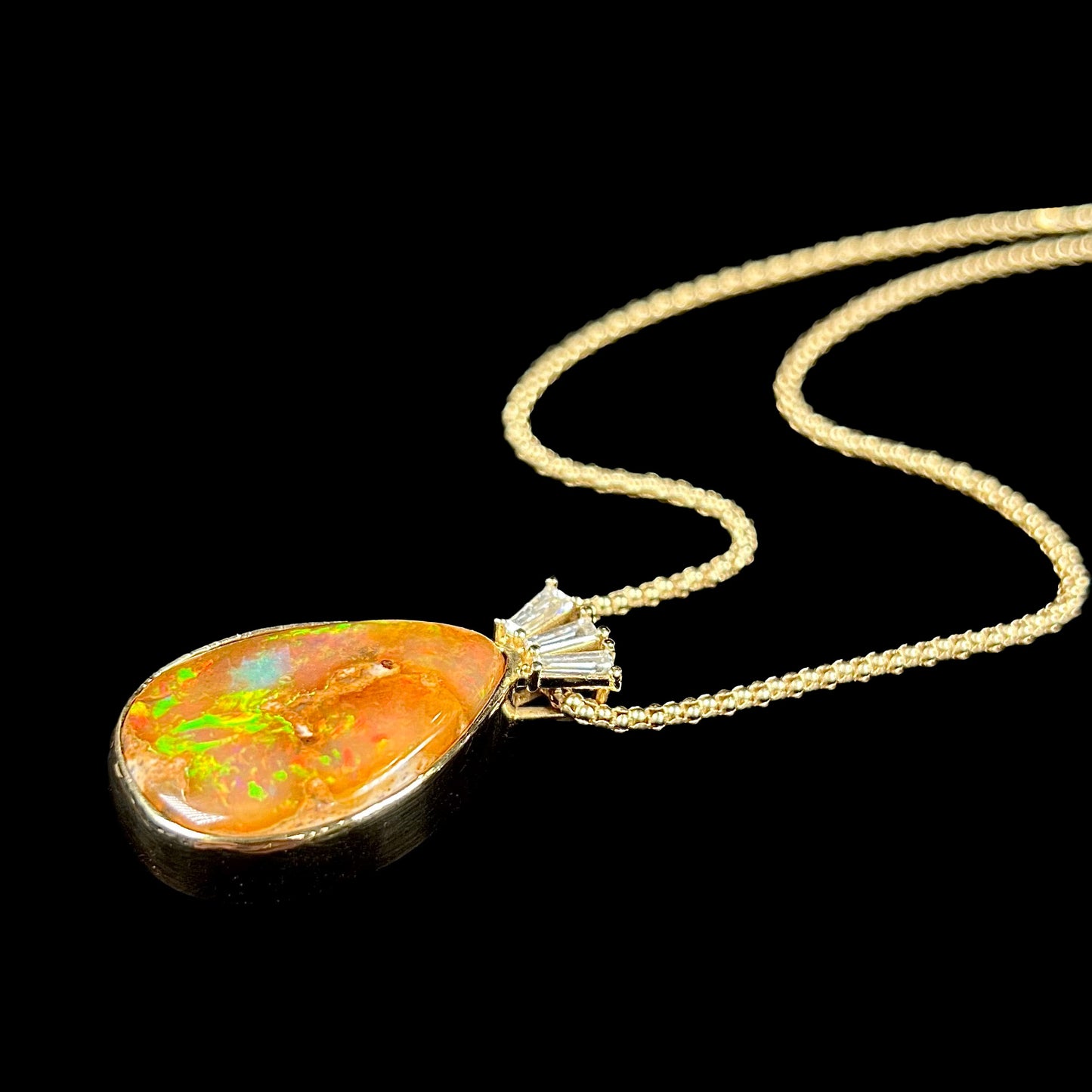 A unisex pear shaped fire opal pendant set with tapered baguette cut diamond accents in 18 karat gold.