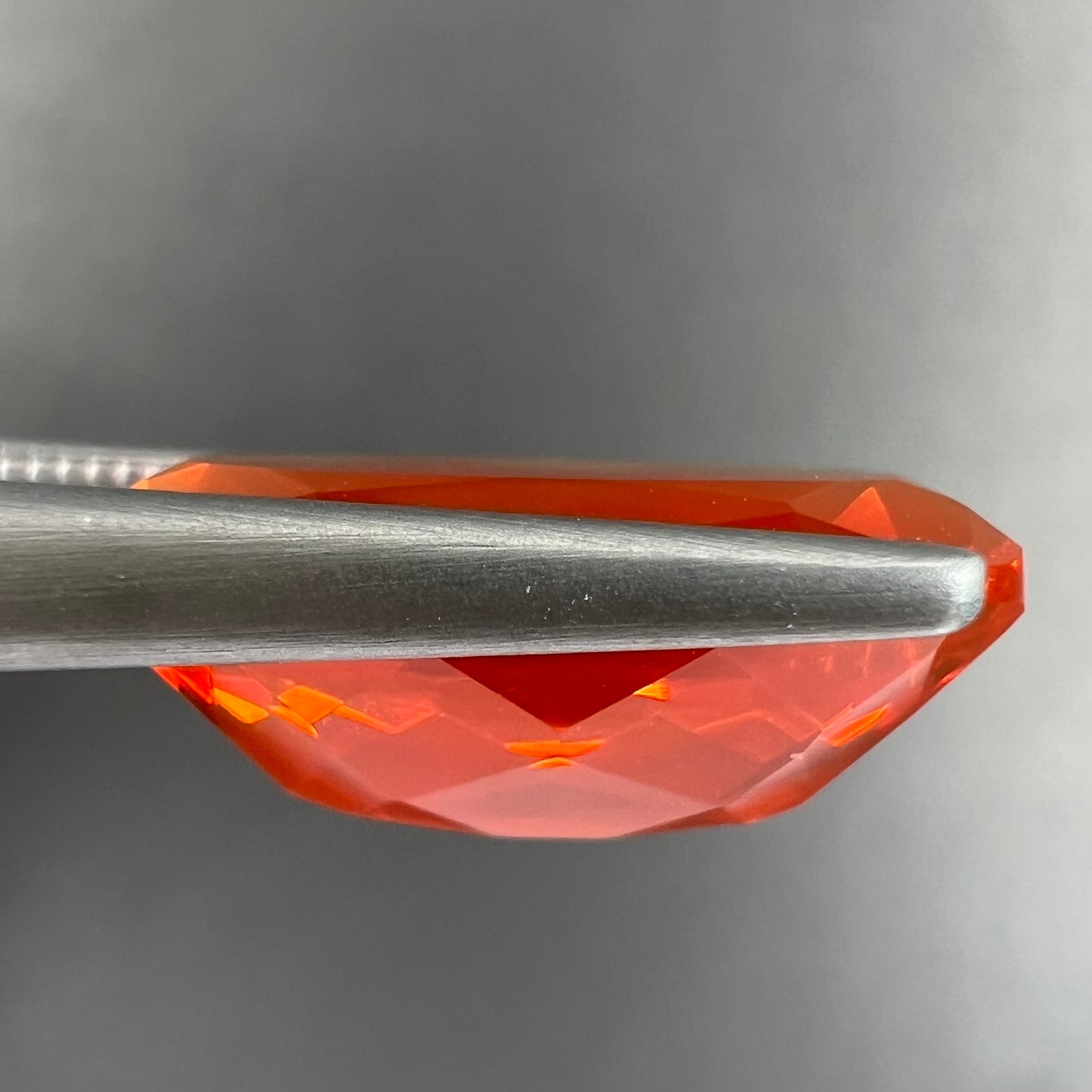 A loose, faceted oval cut Mexican fire opal stone. The stone is a bright orange color.