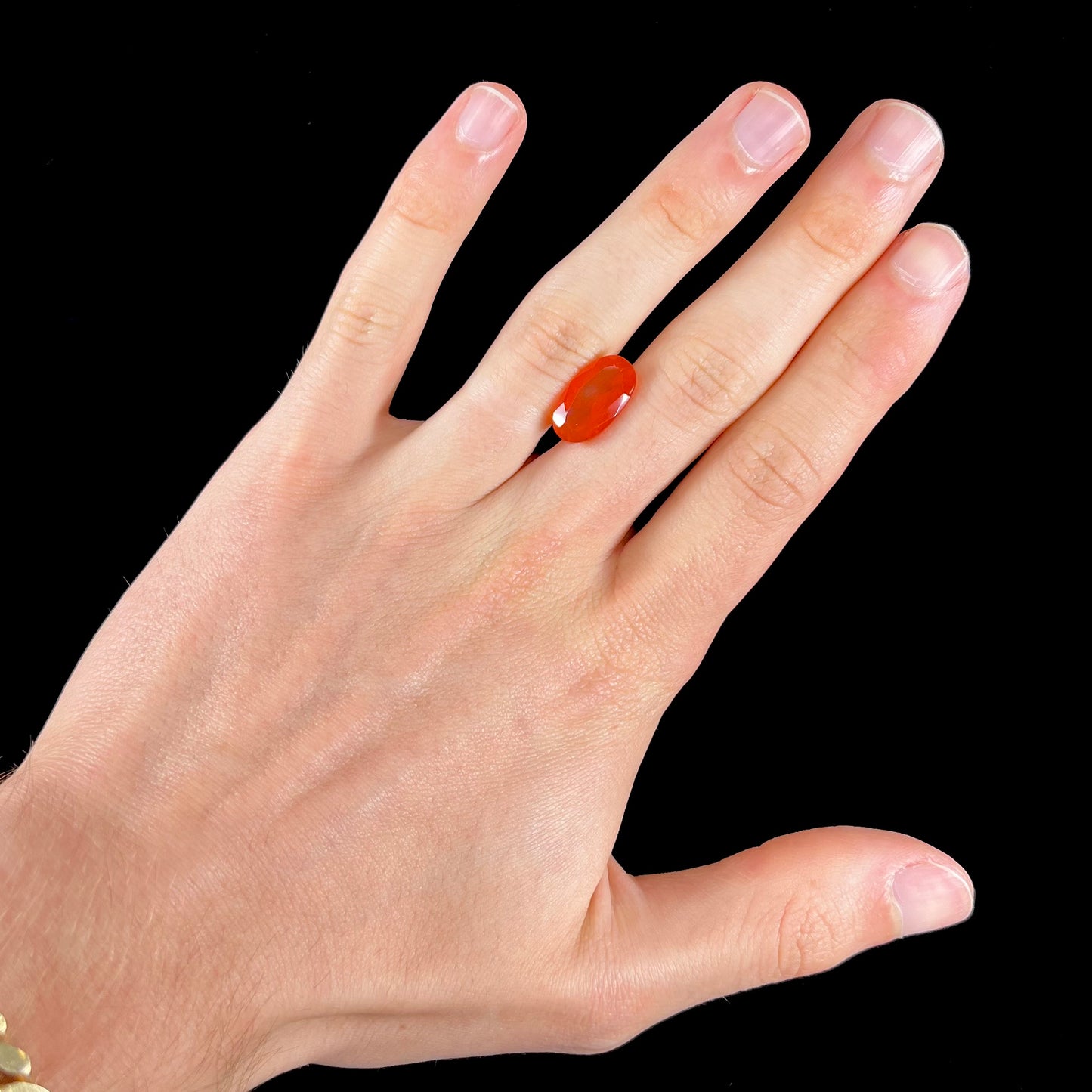 A loose, faceted oval cut Mexican fire opal stone. The stone is a bright orange color.