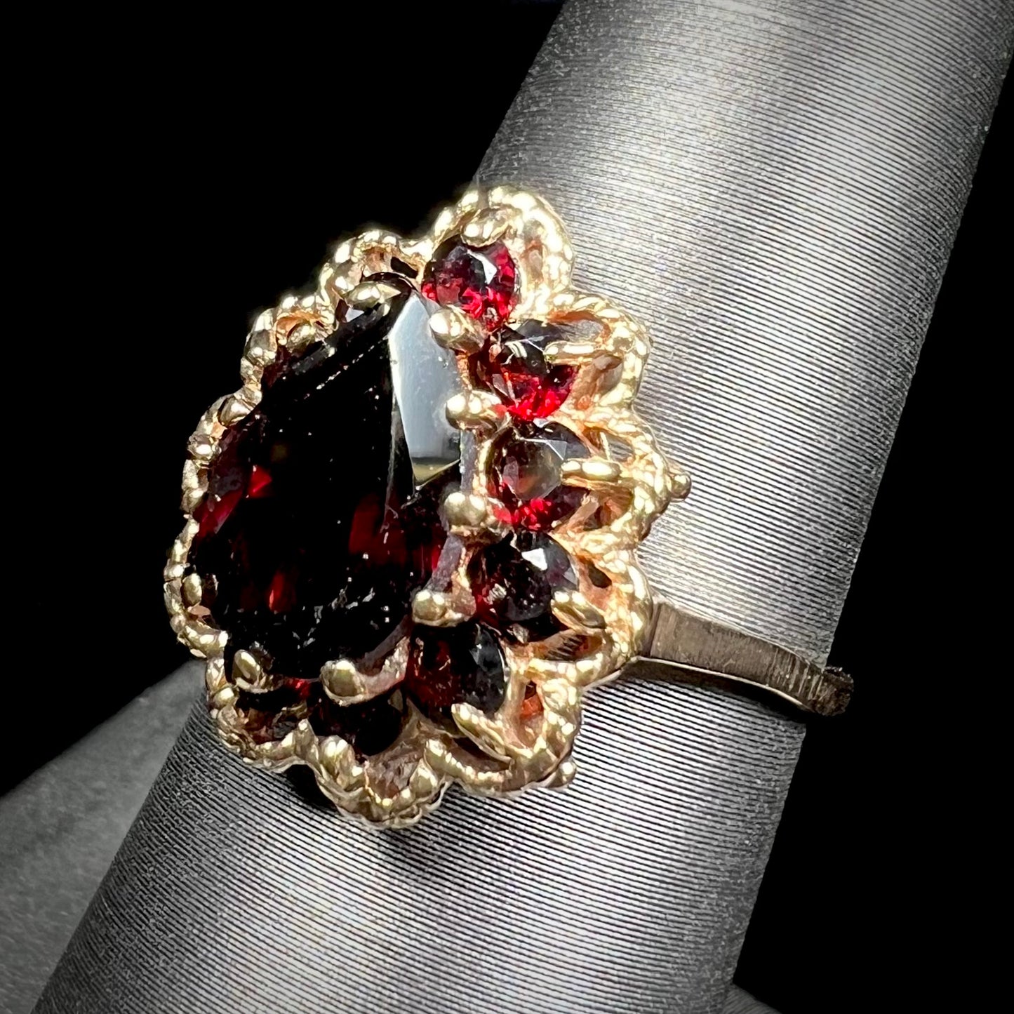 A vintage, 1940's style yellow gold ring set with a pear shaped almandine garnet. A halo of round garnets surround the center stone.