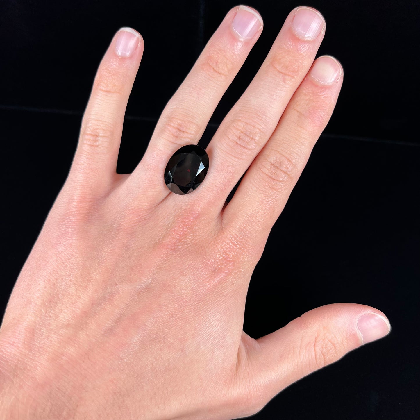 A loose, faceted oval cut pyrope garnet gemstone. The stone is a deep, dark red color.