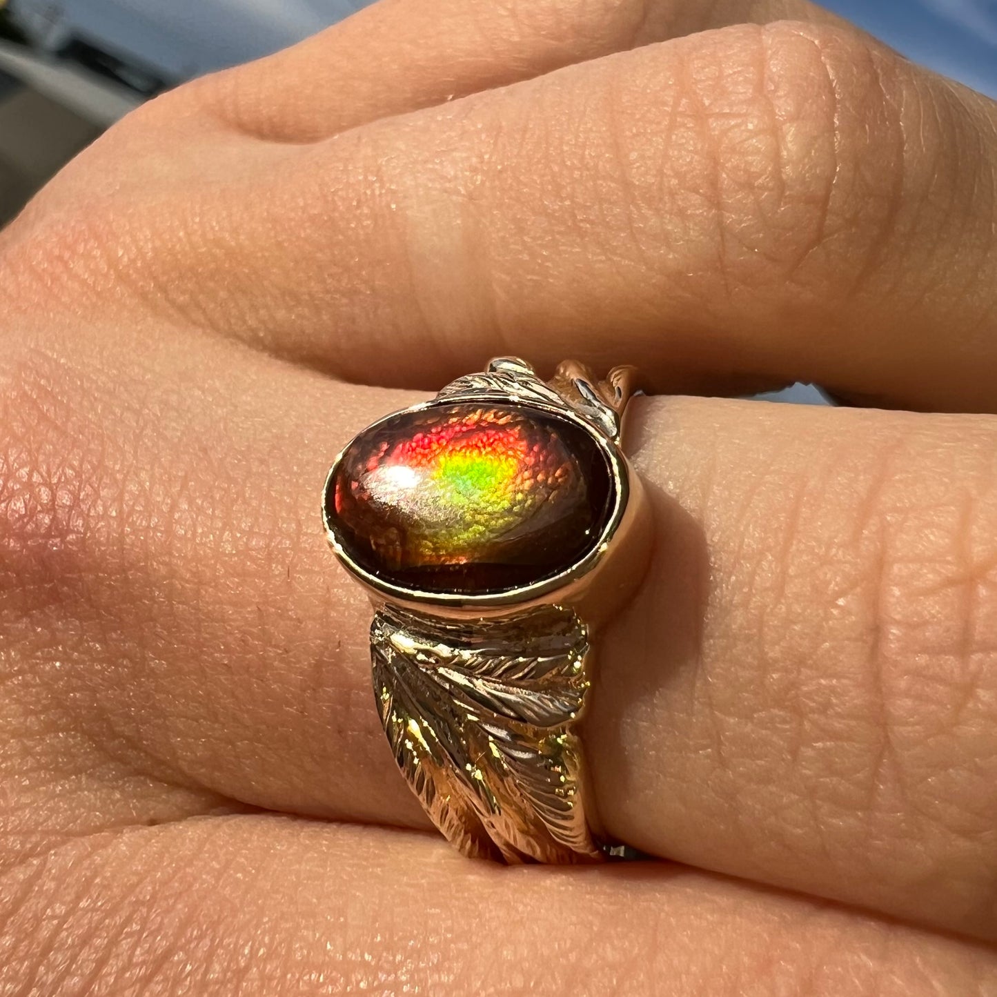 A unisex oval cabochon cut fire agate ring cast in yellow gold. The stone flashes green and red colors.