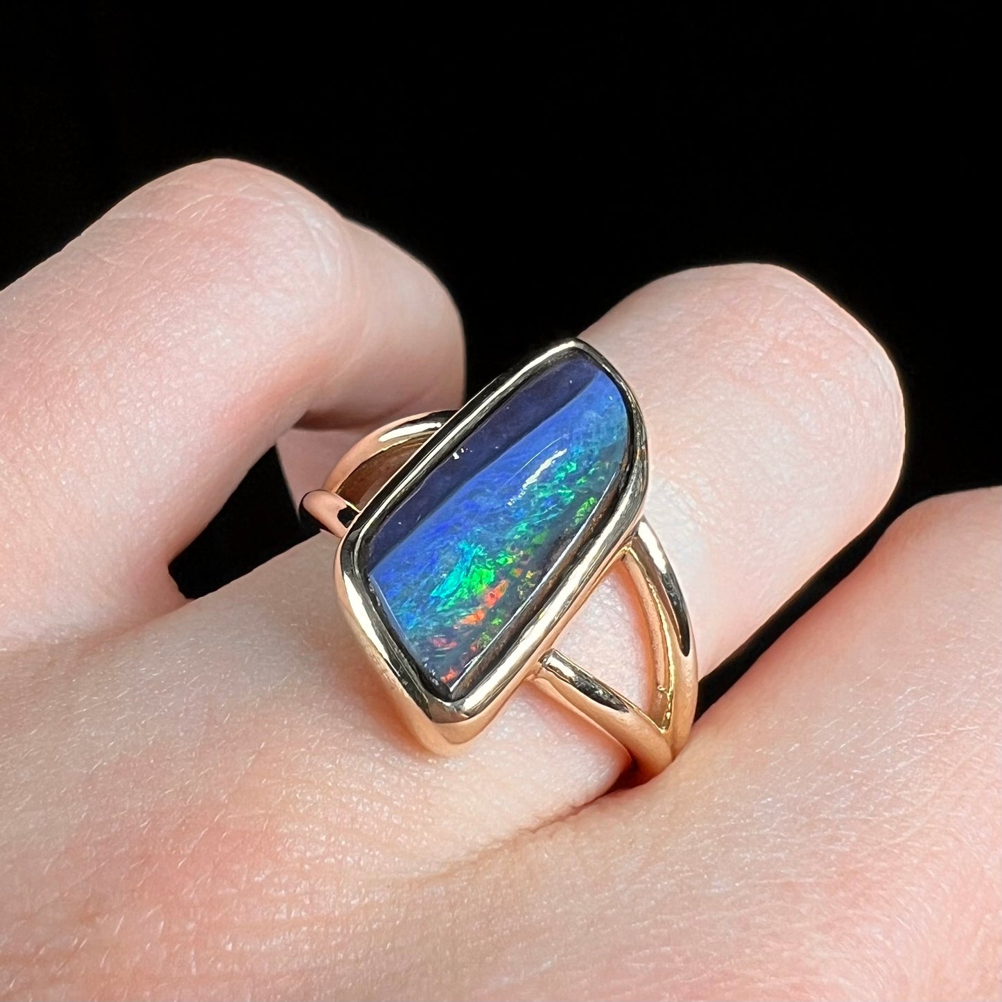 A ladies' split shank gold ring bezel set with a natural, Australian black boulder opal.