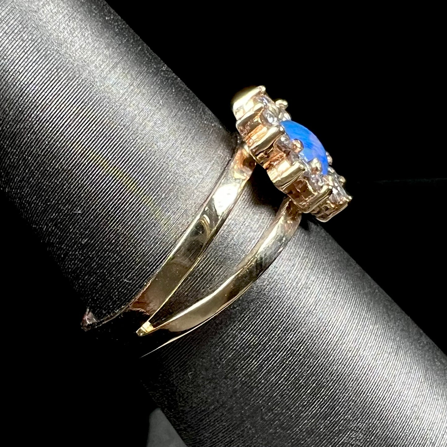 A ladies' round cut black opal and diamond halo ring. The ring is yellow gold and has a split shank.