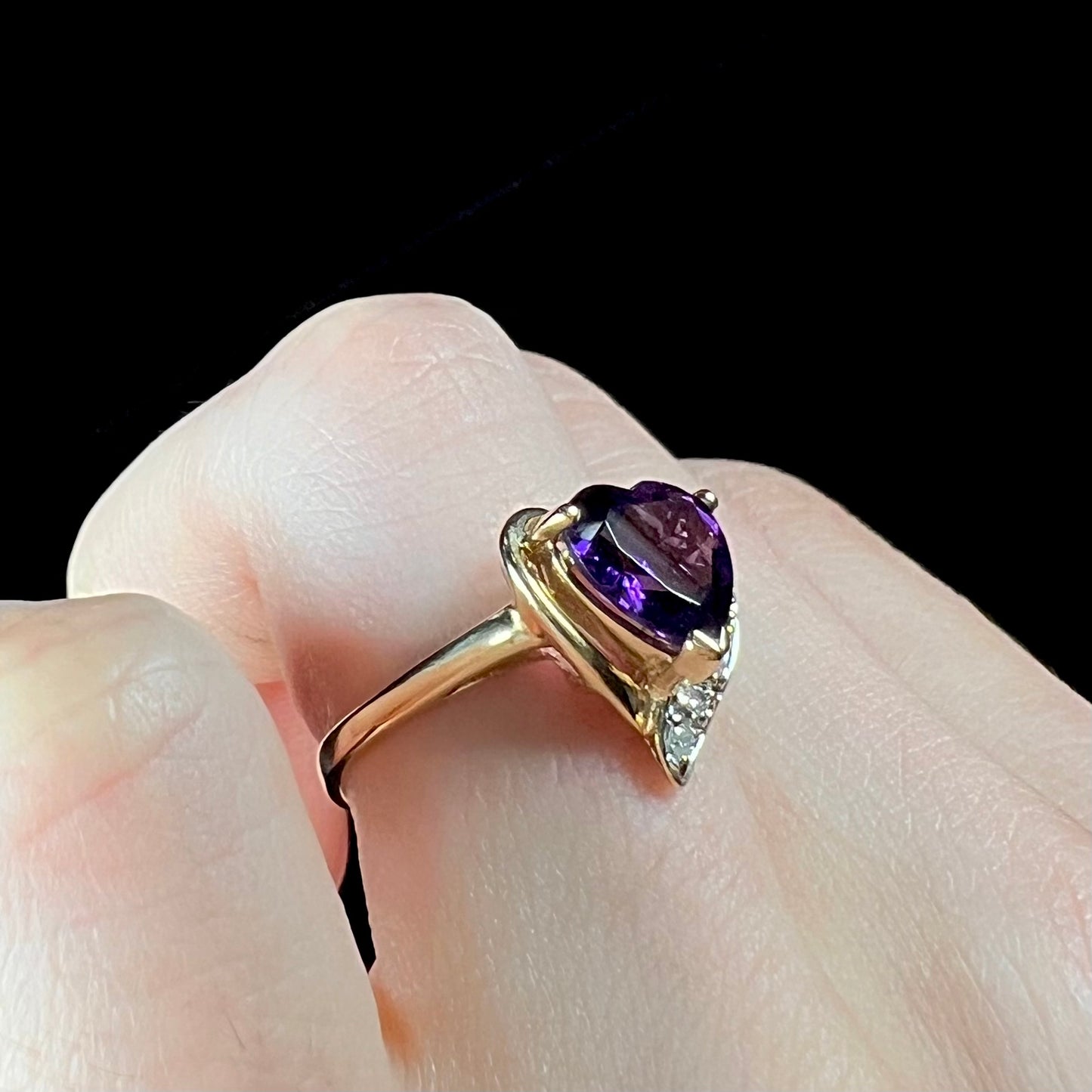 A ladies' yellow gold ring set with a heart shaped amethyst and round cut diamond accents.