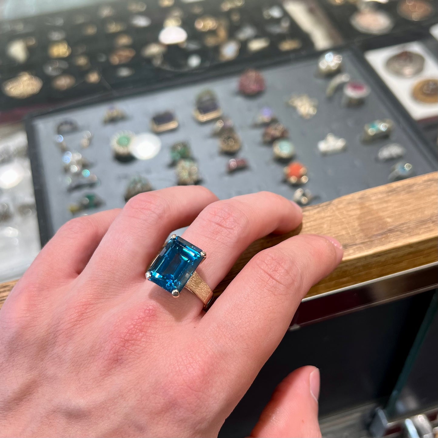 A ladies' yellow gold London blue topaz solitaire ring. The ring is textured, and the topaz is emerald cut.