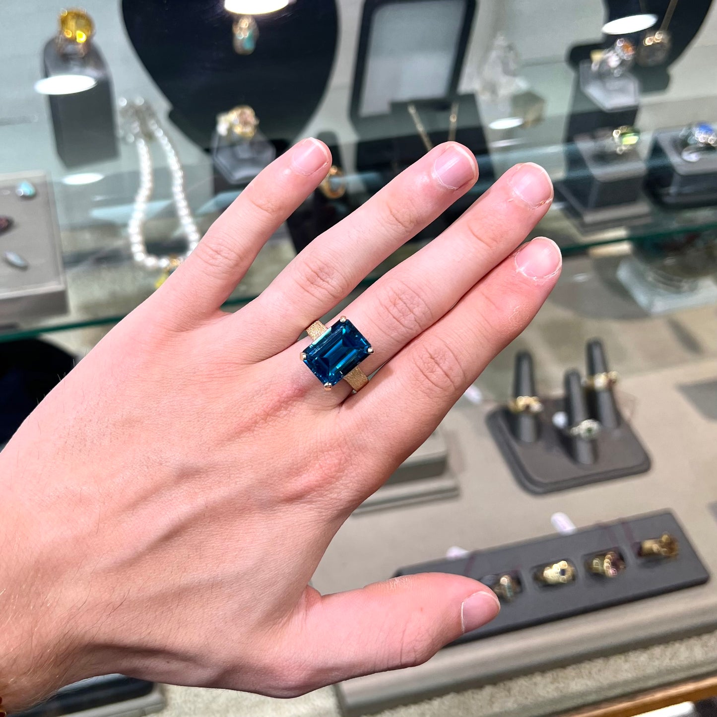 A ladies' yellow gold London blue topaz solitaire ring. The ring is textured, and the topaz is emerald cut.