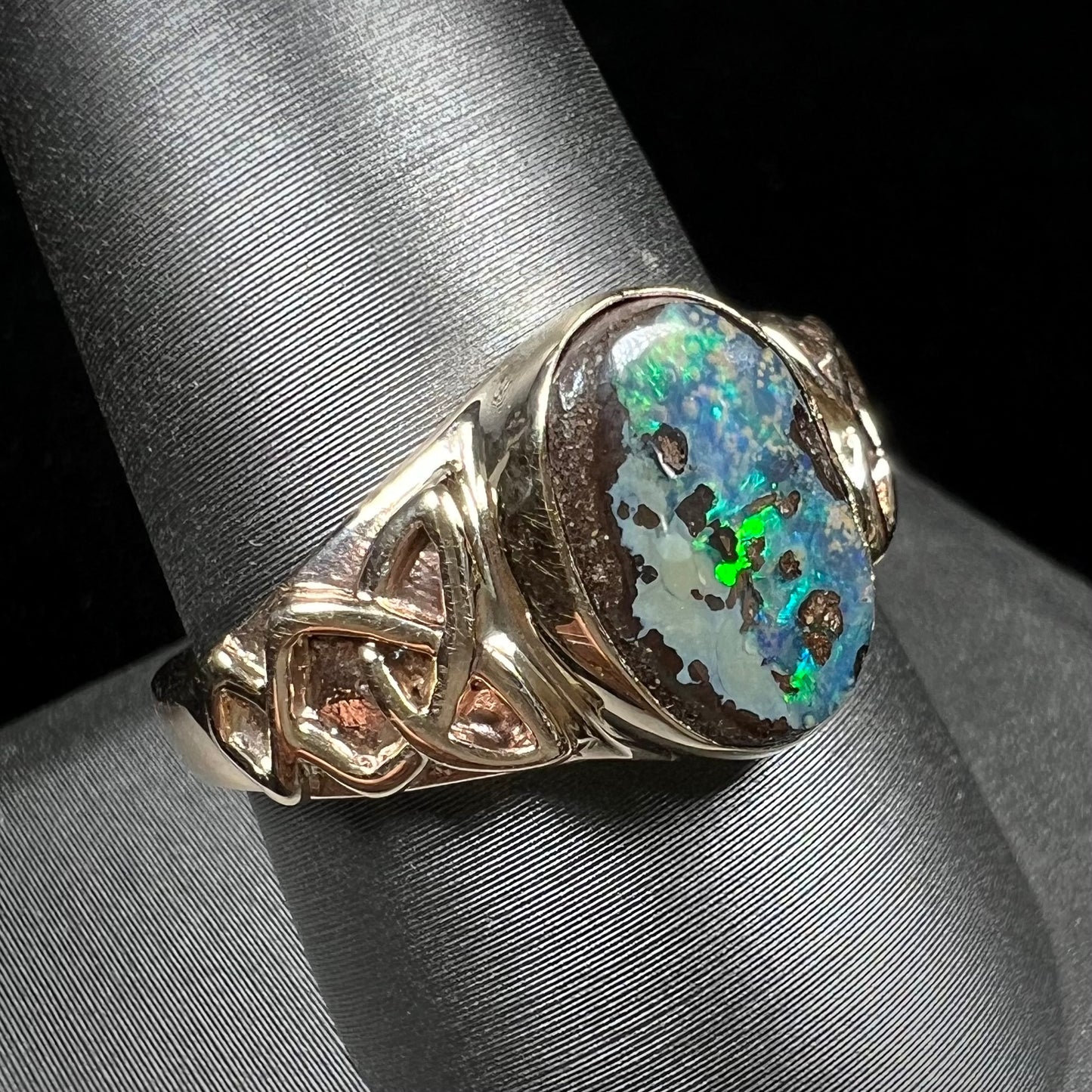 A unisex Celtic style natural boulder opal ring cast in yellow gold. The opal shines green and blue.