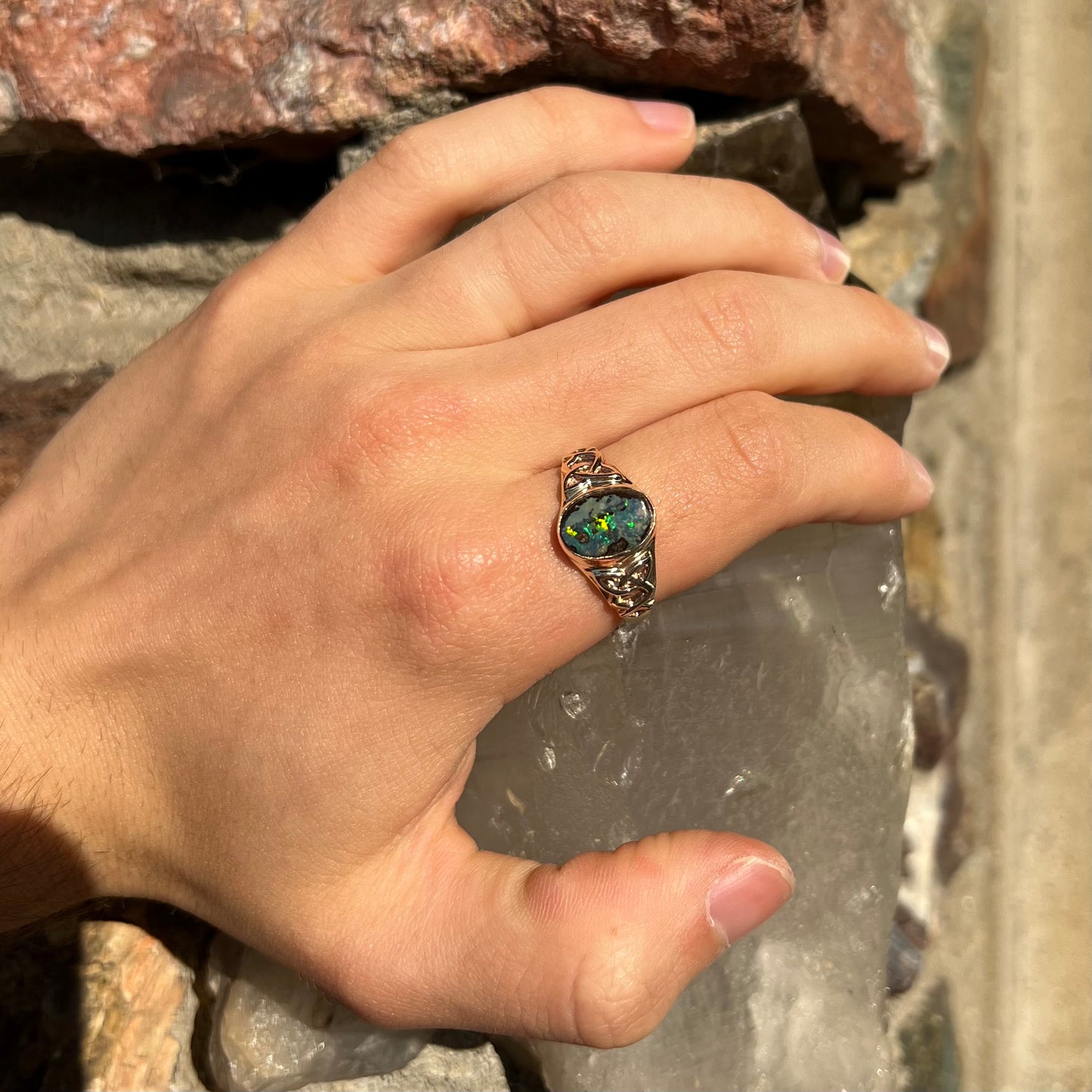 A unisex Celtic style natural boulder opal ring cast in yellow gold. The opal shines green and blue.