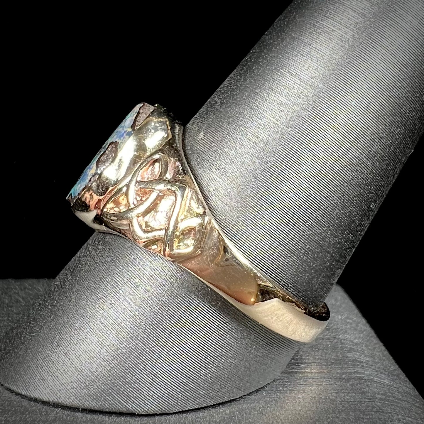 A unisex Celtic style natural boulder opal ring cast in yellow gold. The opal shines green and blue.