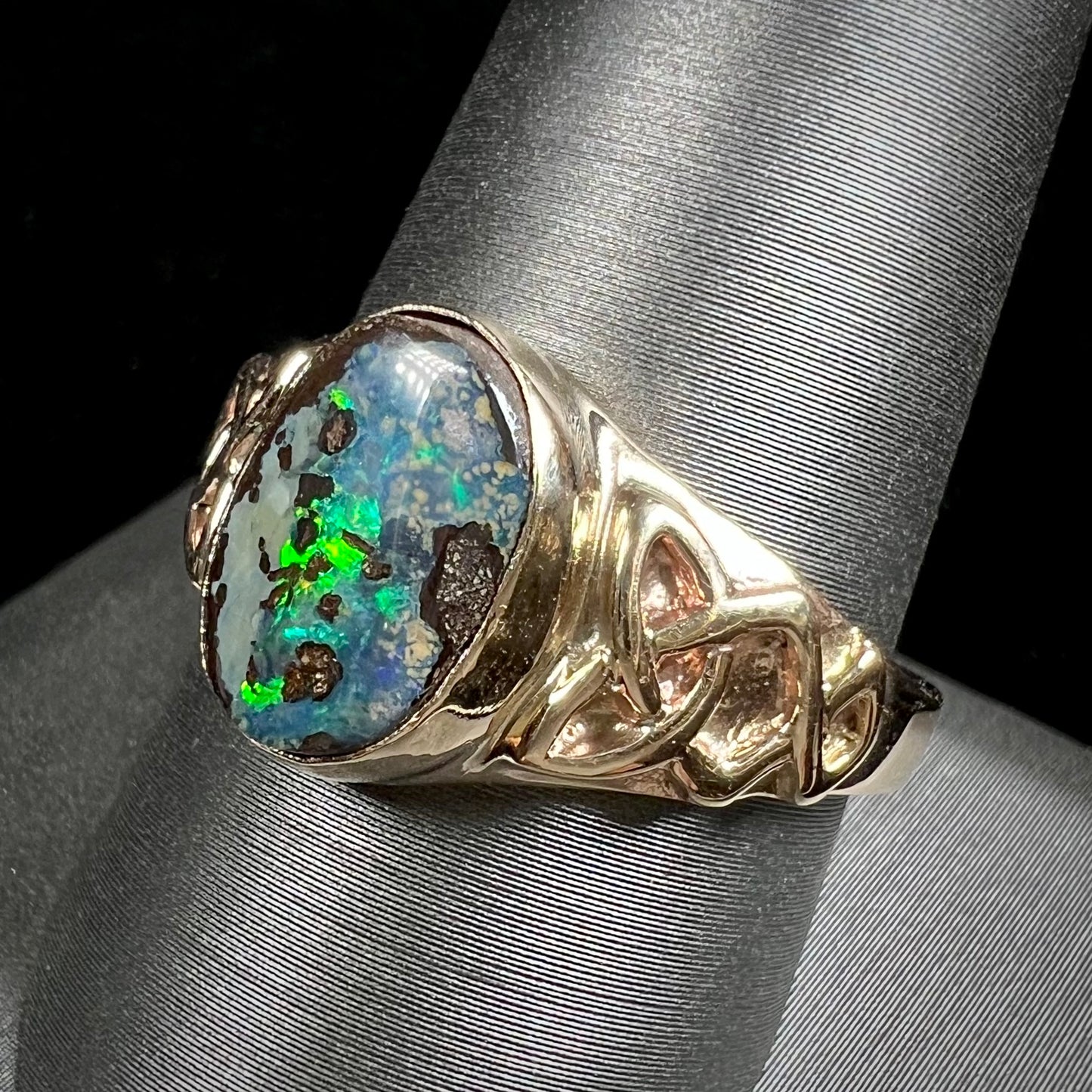 A unisex Celtic style natural boulder opal ring cast in yellow gold. The opal shines green and blue.