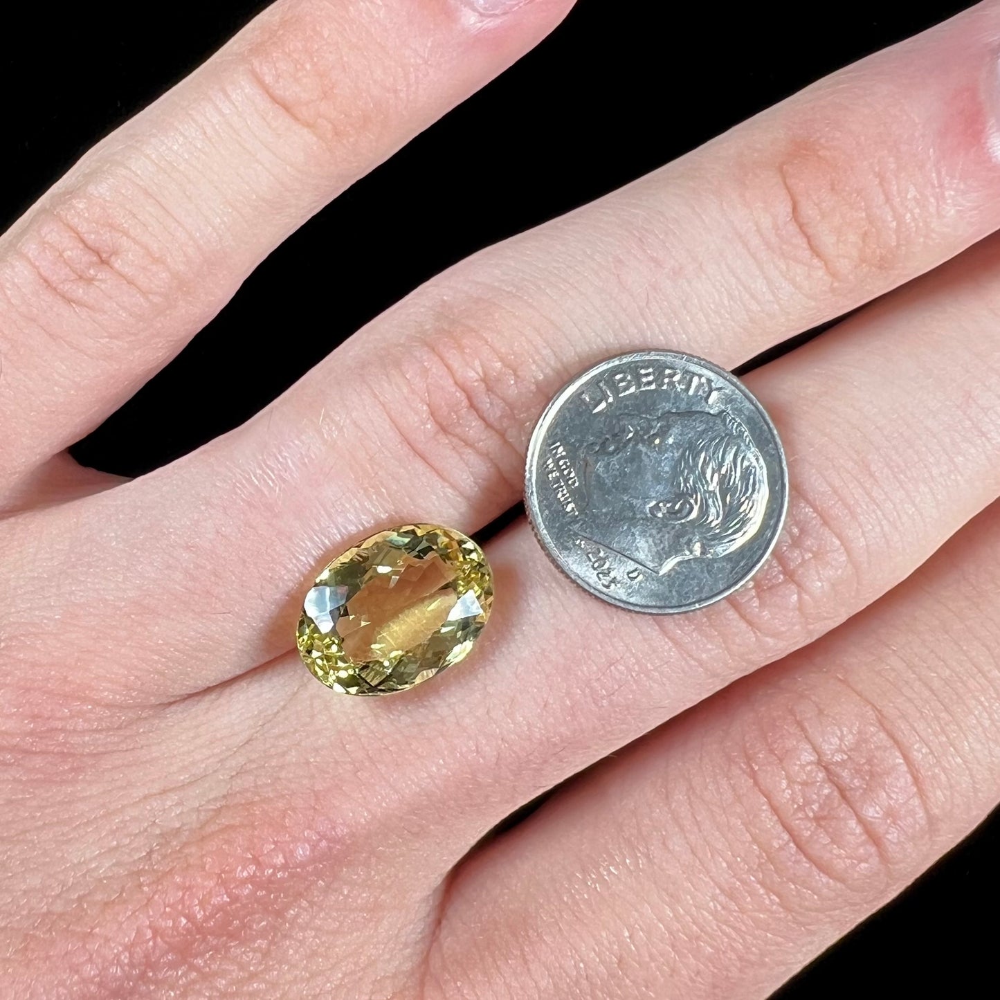 A faceted oval cut golden beryl gemstone. The stone is a greenish light yellow.