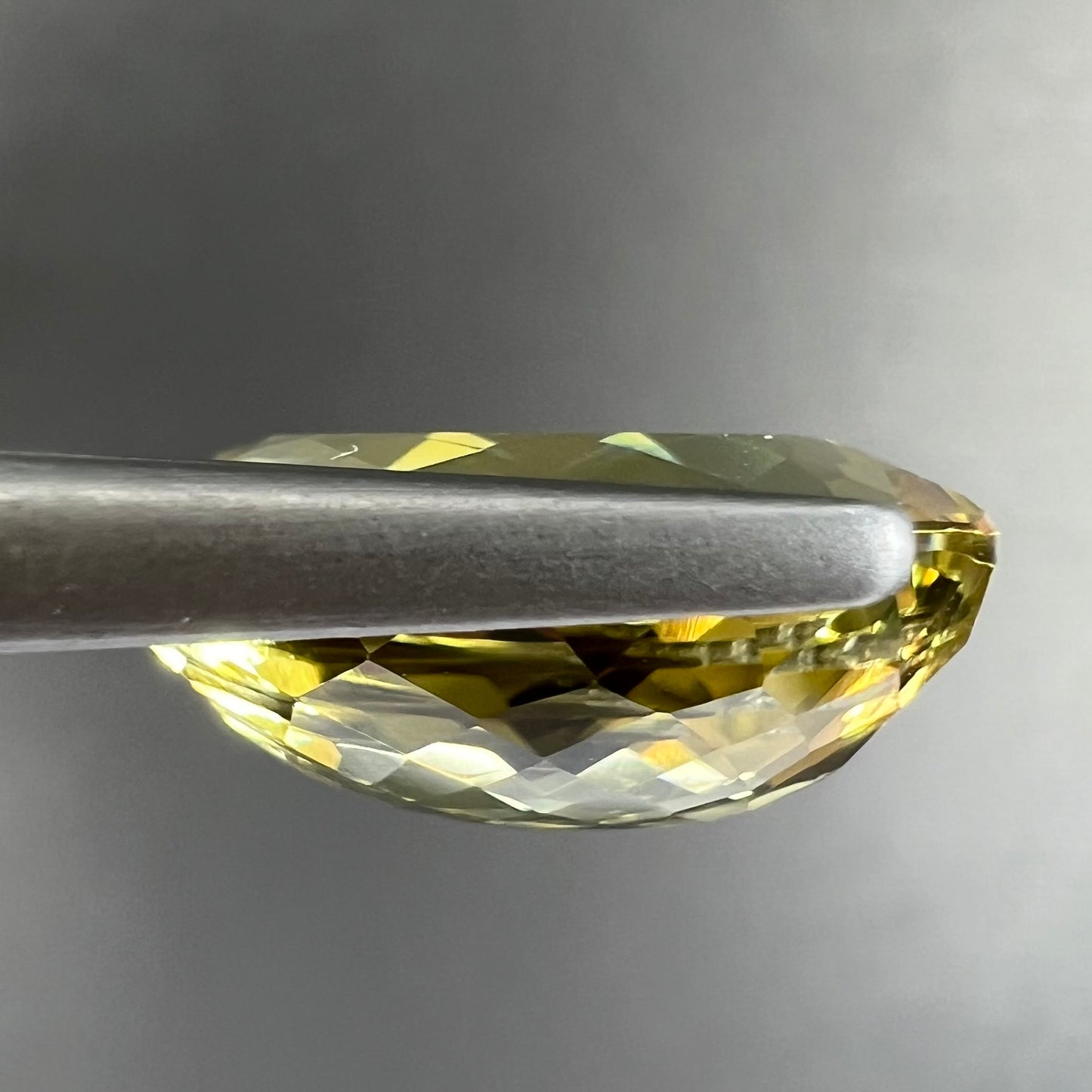 A faceted oval cut golden beryl gemstone. The stone is a greenish light yellow.