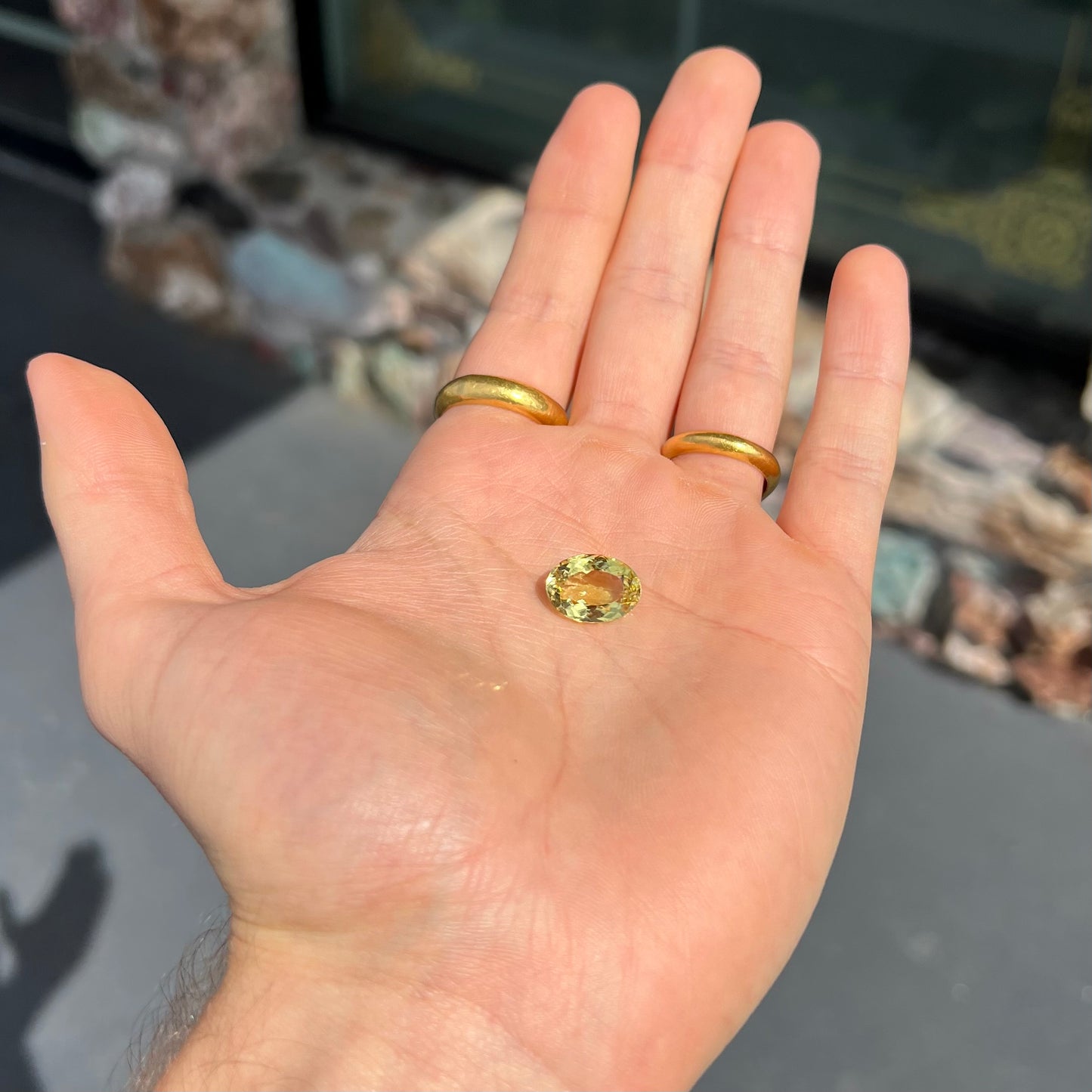 A faceted oval cut golden beryl gemstone. The stone is a greenish light yellow.