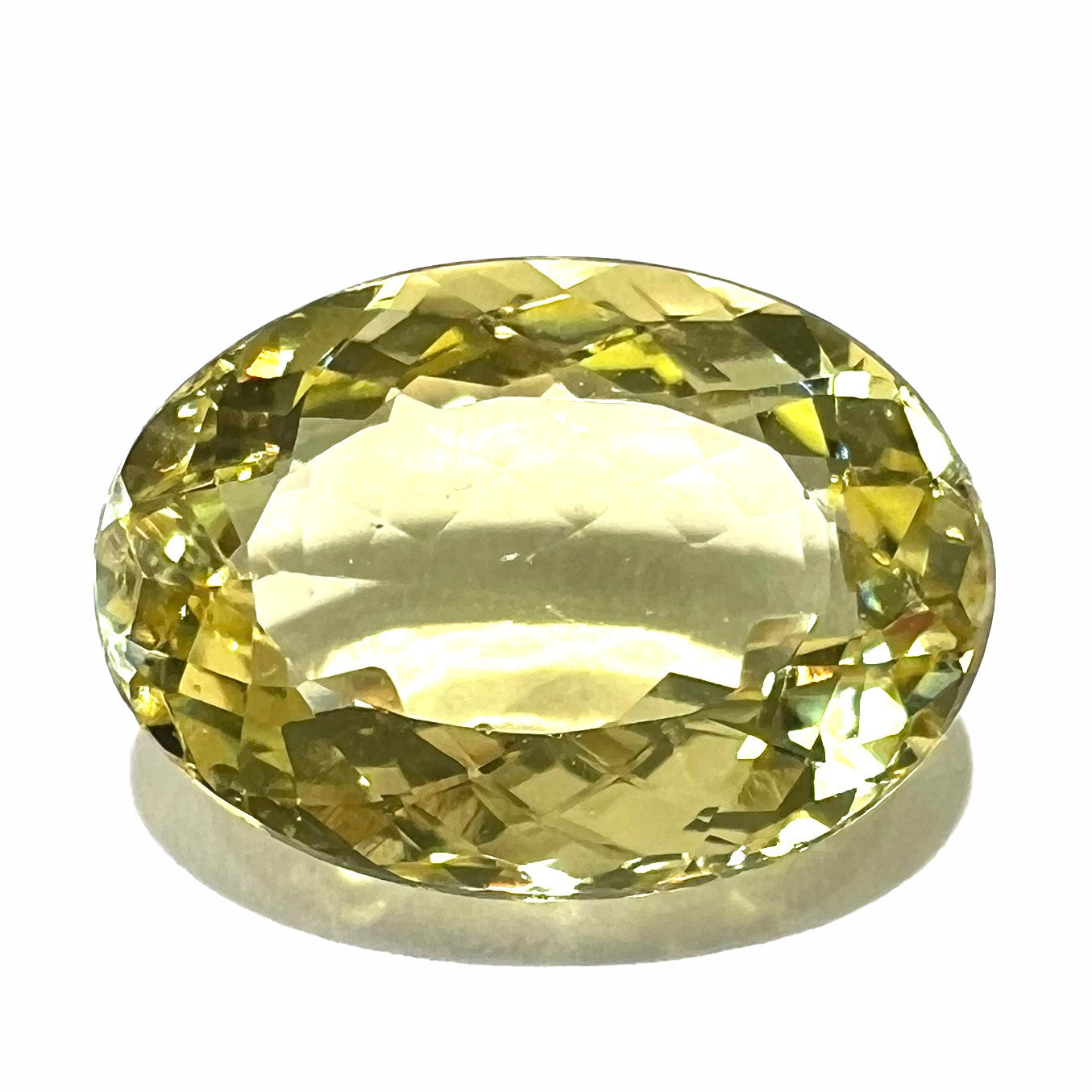 A faceted oval cut golden beryl gemstone. The stone is a greenish light yellow.