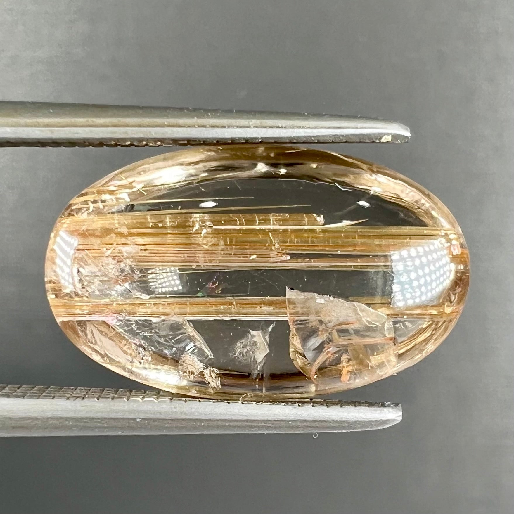 A loose, oval cabochon cut cat's eye golden rutilated quartz stone.