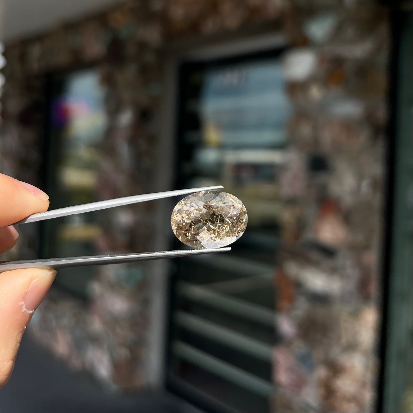 A faceted oval cut rutilated quartz gemstone. The stone is smoky color with golden rutile needle inclusions.