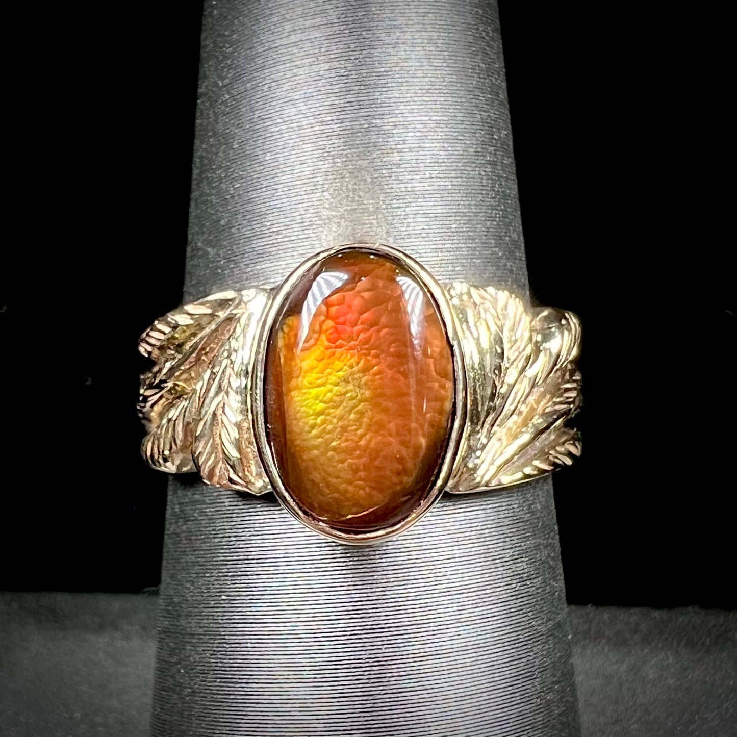 A unisex oval cabochon cut fire agate ring cast in yellow gold. The stone flashes green and red colors.
