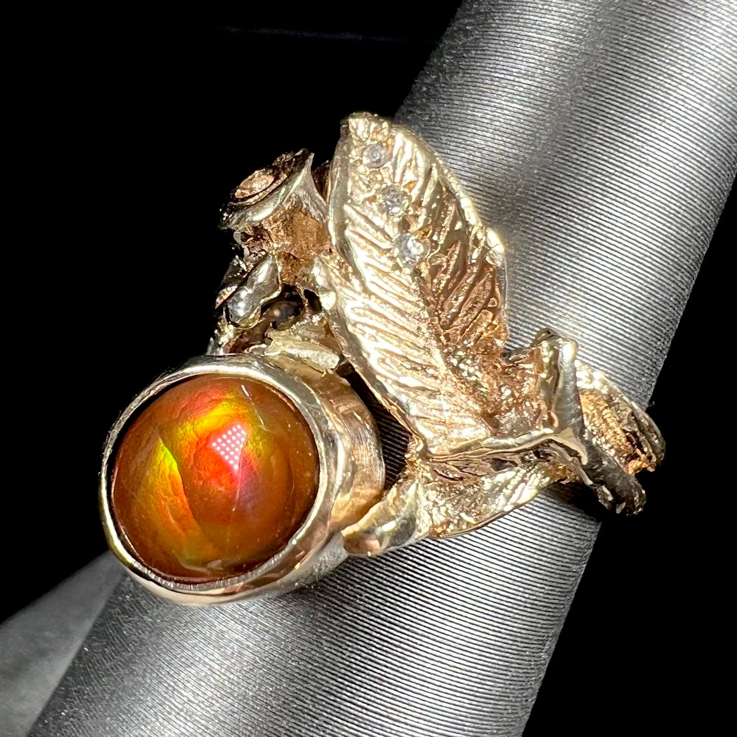 A ladies' yellow gold flower style ring set with an oval cabochon cut fire agate and diamond accents.