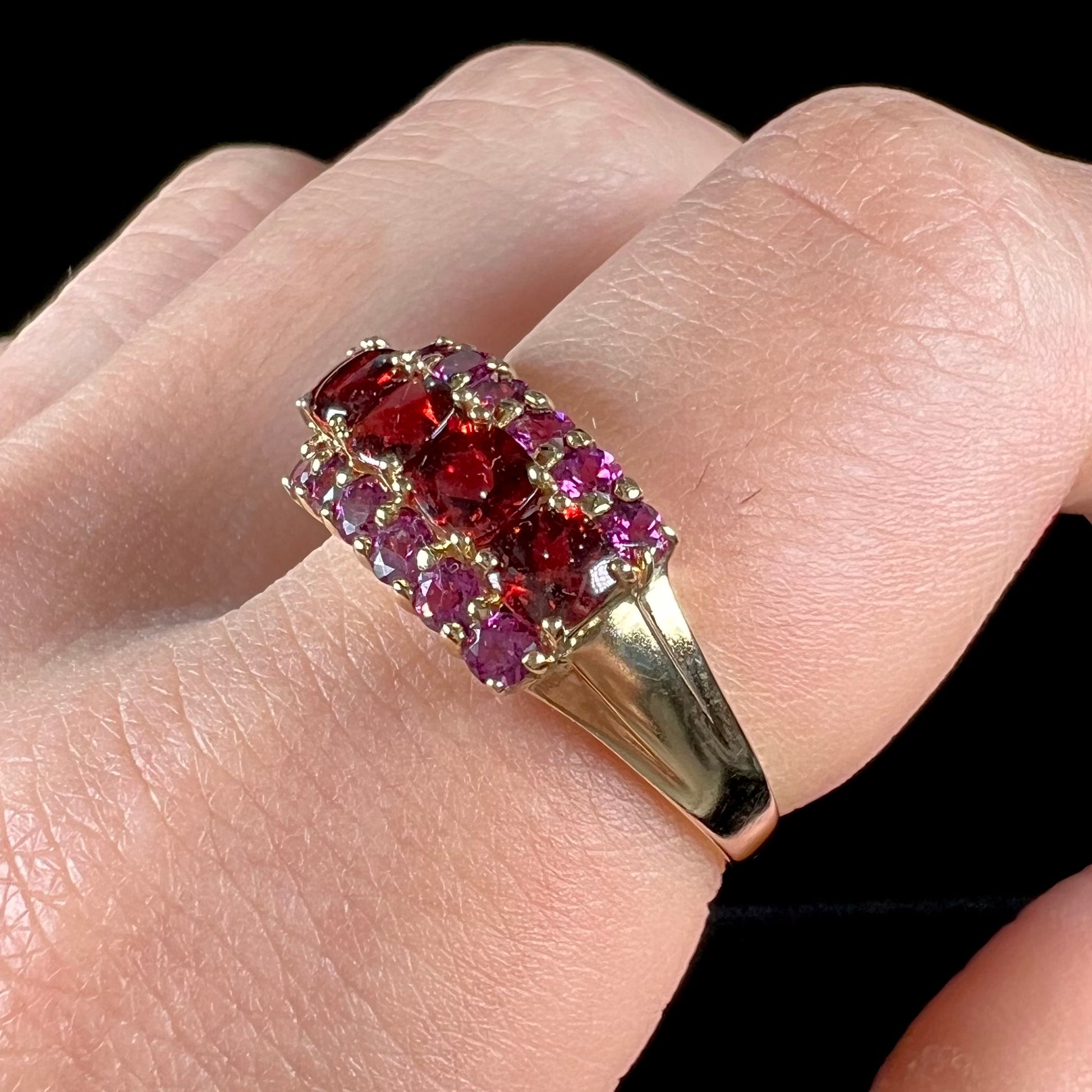 A gold ring set with buff cut cushion shaped almandine garnets with round cut purple rhodolite garnet accents.