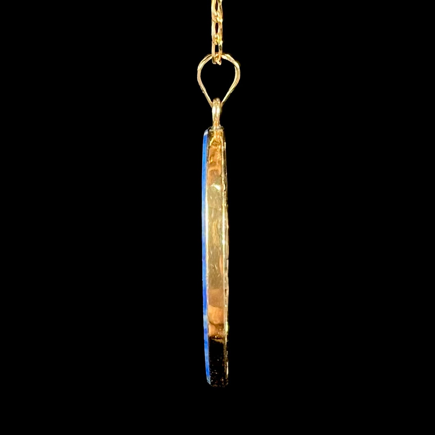 An oval cut lapis lazuli pendant set in a yellow gold frame featuring the design of two swans swimming in a pond.