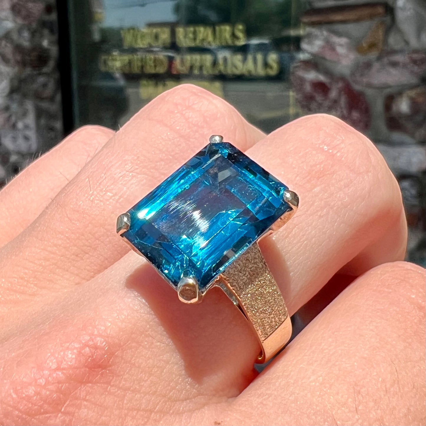 A ladies' yellow gold London blue topaz solitaire ring. The ring is textured, and the topaz is emerald cut.