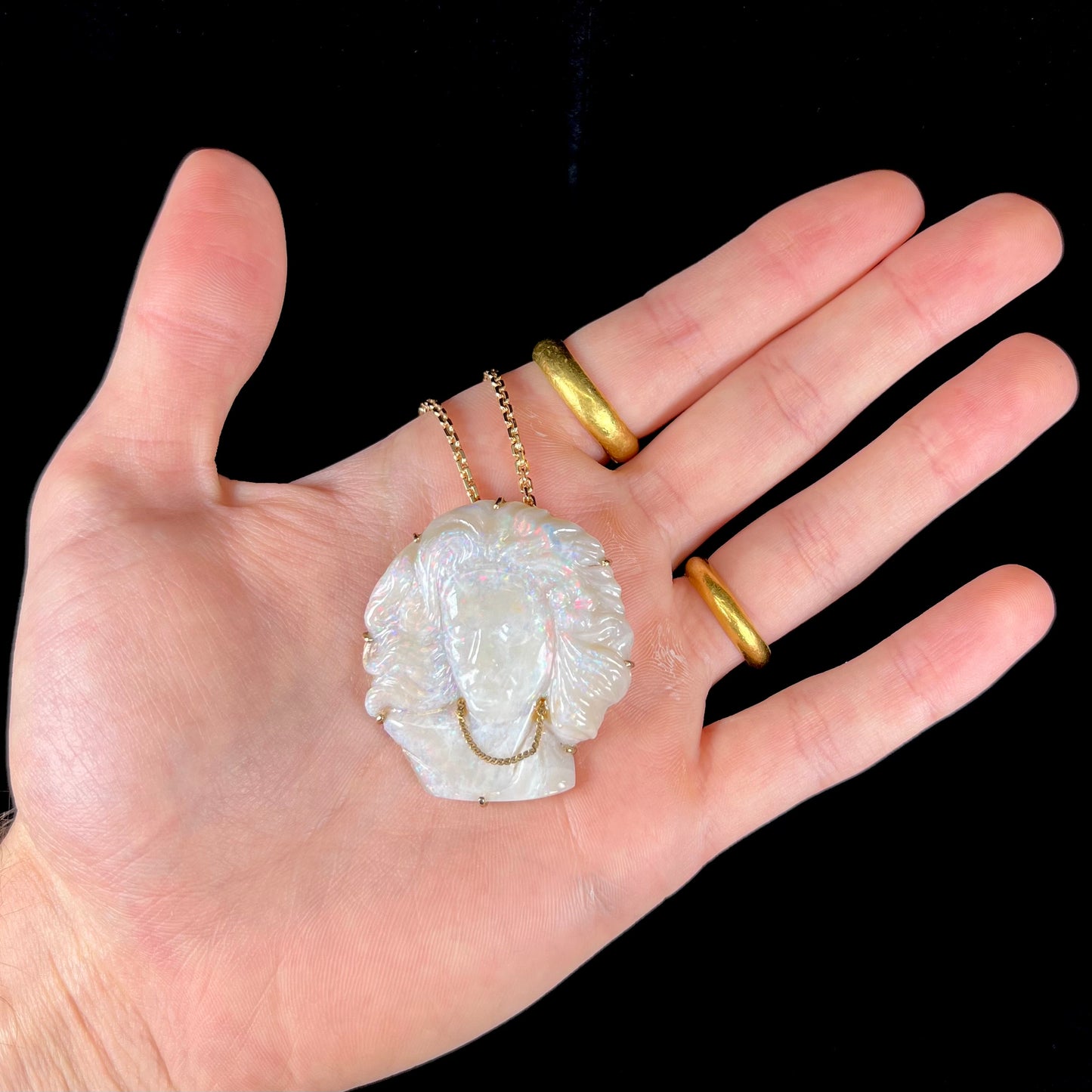 A cameo necklace carved by white crystal opal and held with gold prongs. The cameo is wearing a gold chain.