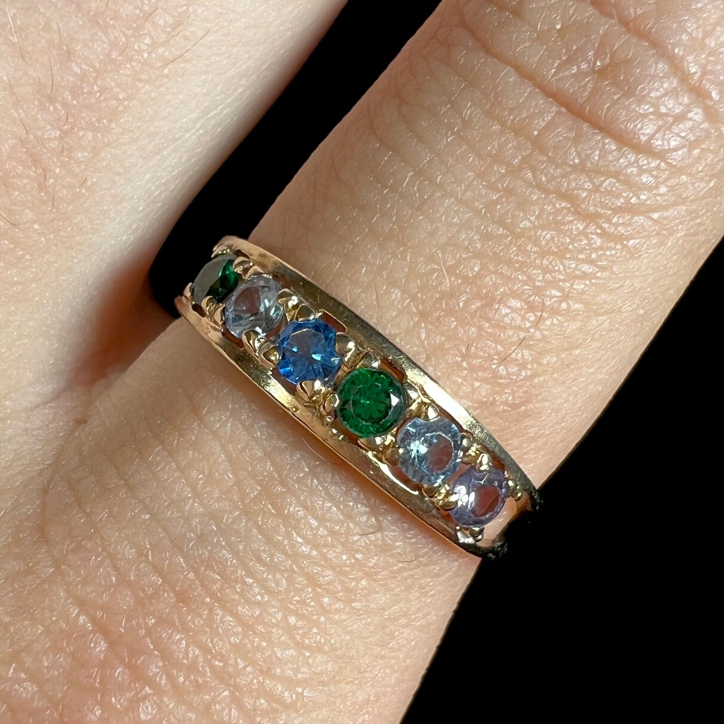 A ladies' yellow gold band set with green, dark blue, light blue, and light purple stones.